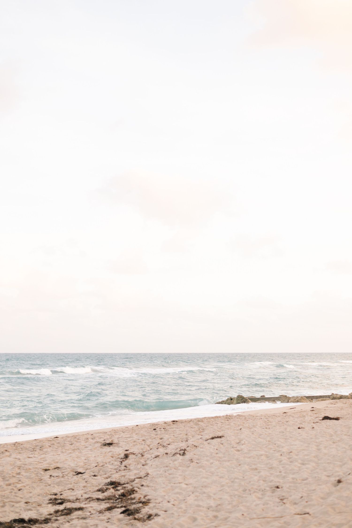 A serene beach landscape with gentle waves rolling onto sandy shores under a soft pastel sky.