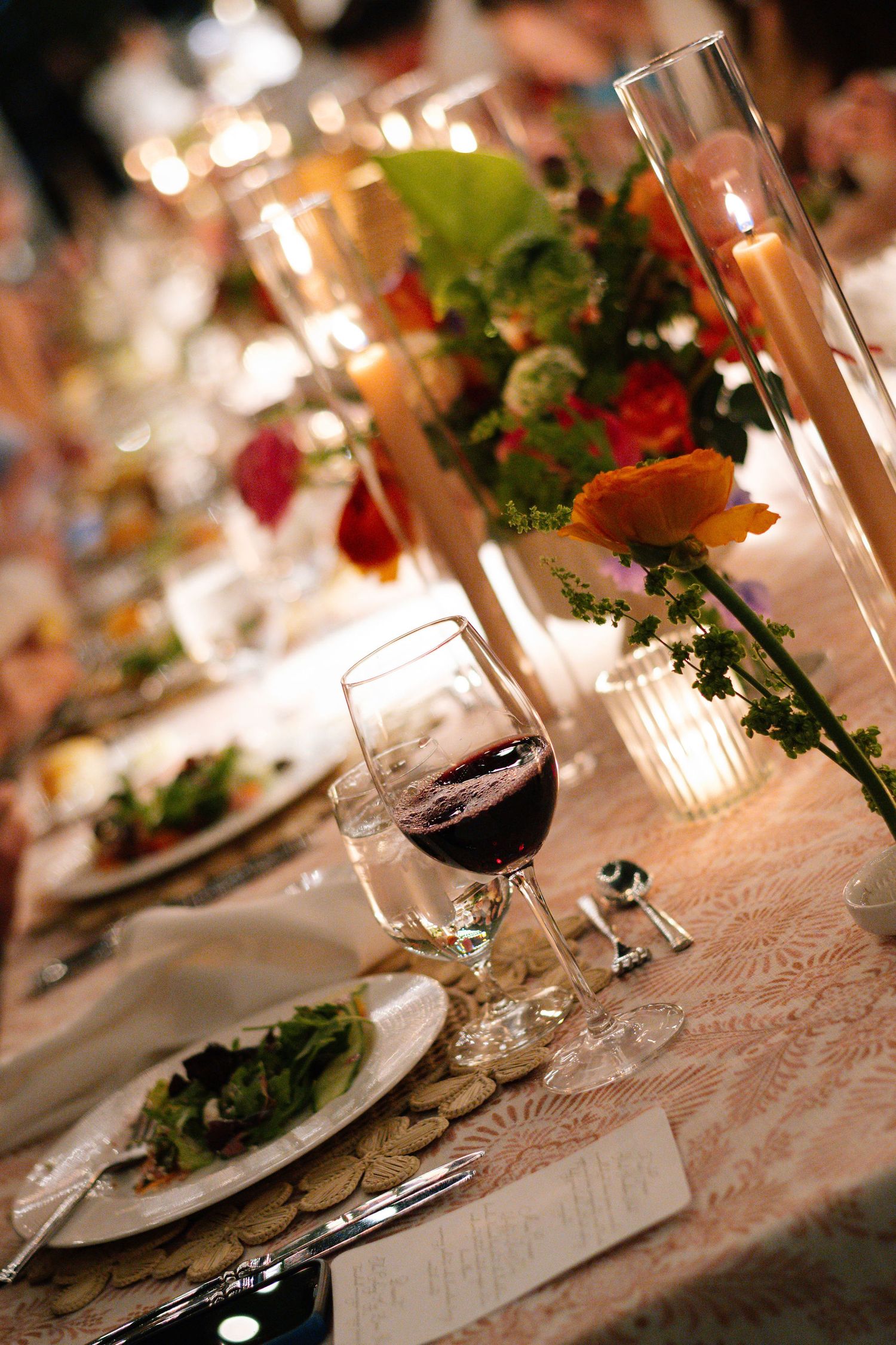 Wedding table settings with glowing candles and floral arrangements on lace tablecloth.