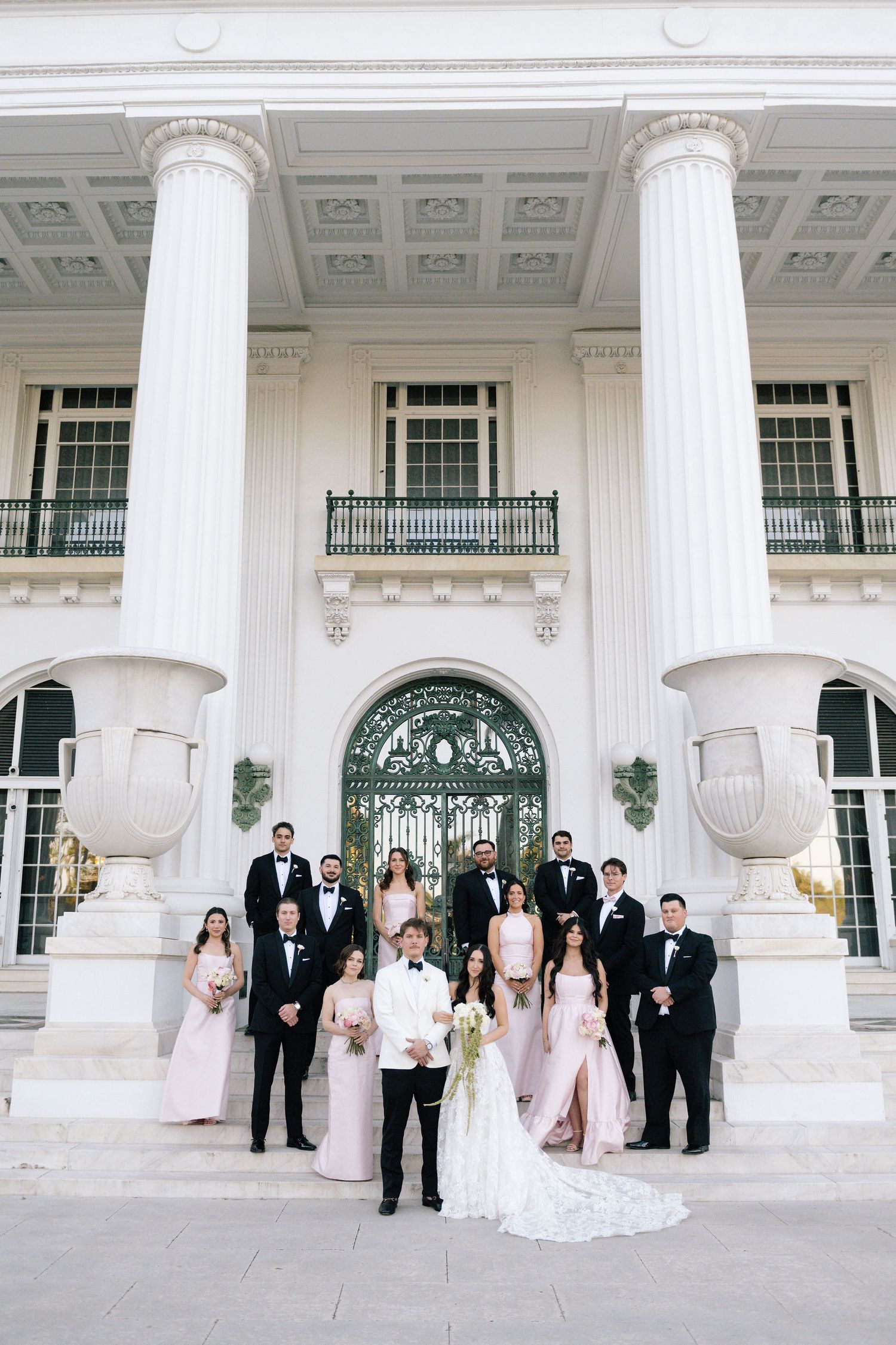 Wedding group photos taken in front of a grand white columned building entrance.