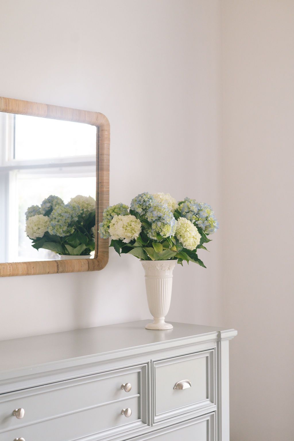 White dresser with hydrangea flowers in vase and mirror decor creating an elegant nursery display.