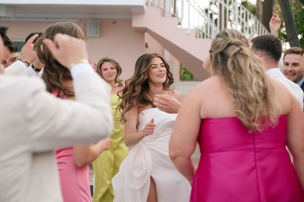 Guests in bright pink dresses and white attire dancing at a wedding reception.