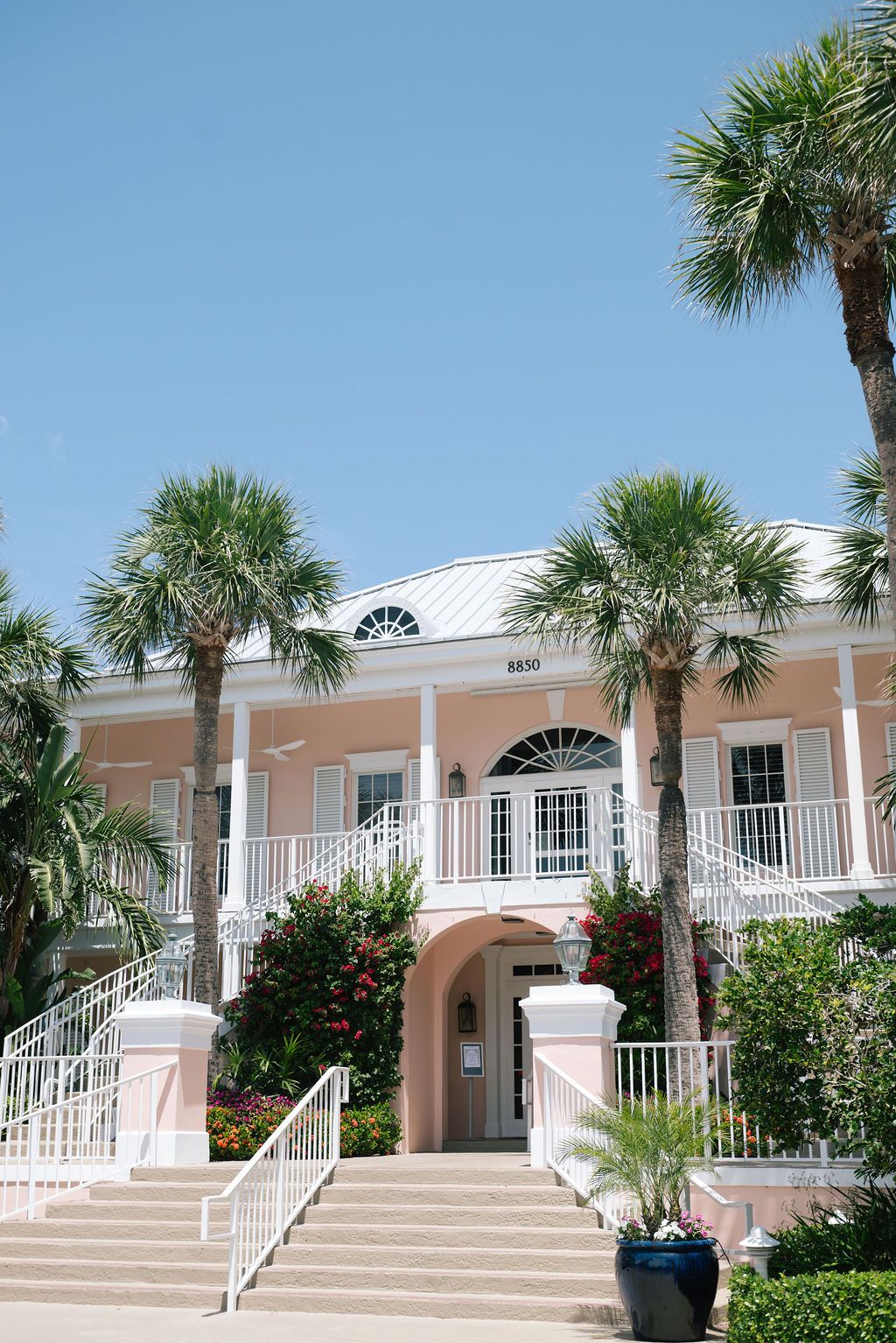 Pink stucco building with white columns and palm trees creates a tropical wedding venue backdrop.