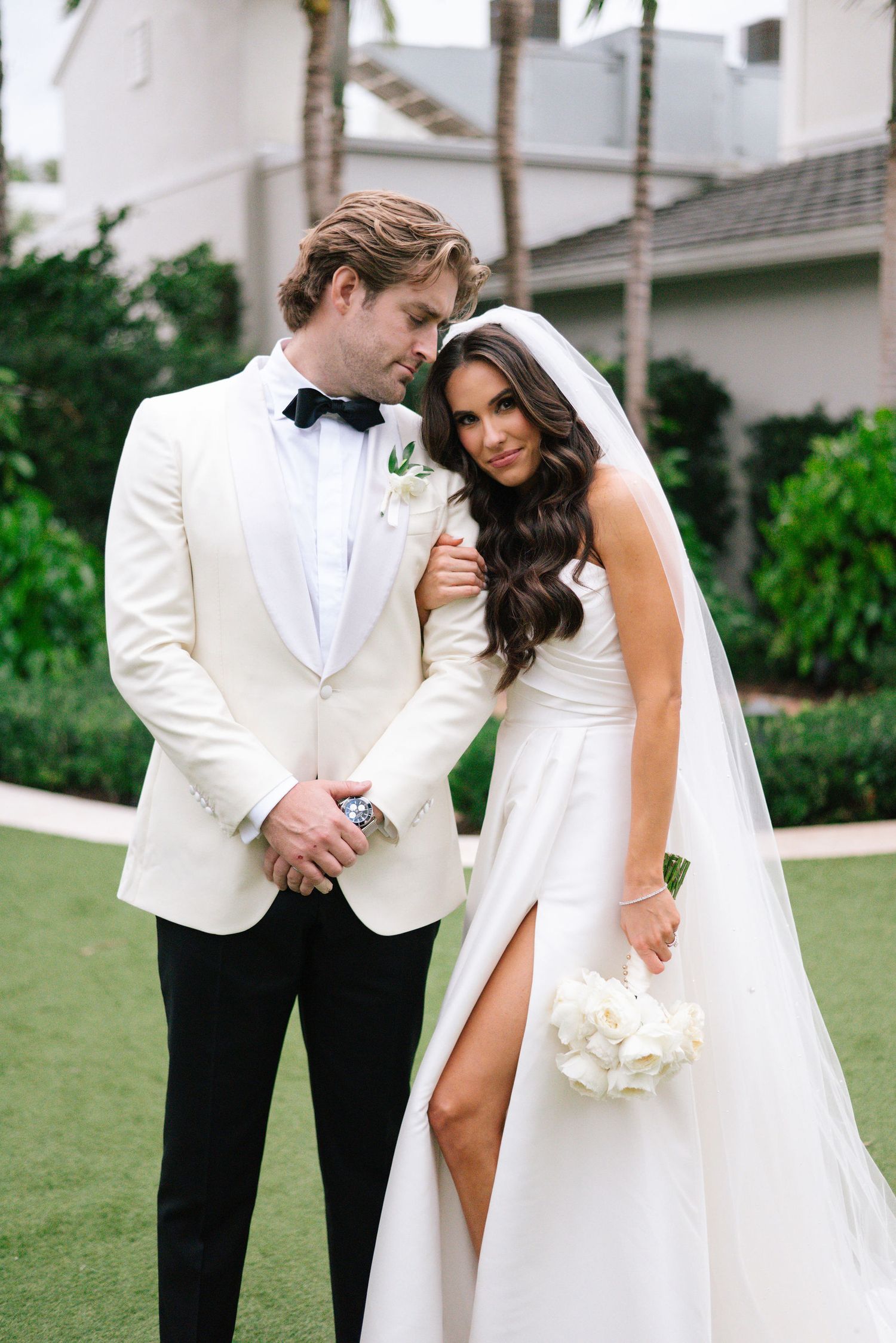 A tender wedding moment captured against a backdrop of palm trees and white architecture.