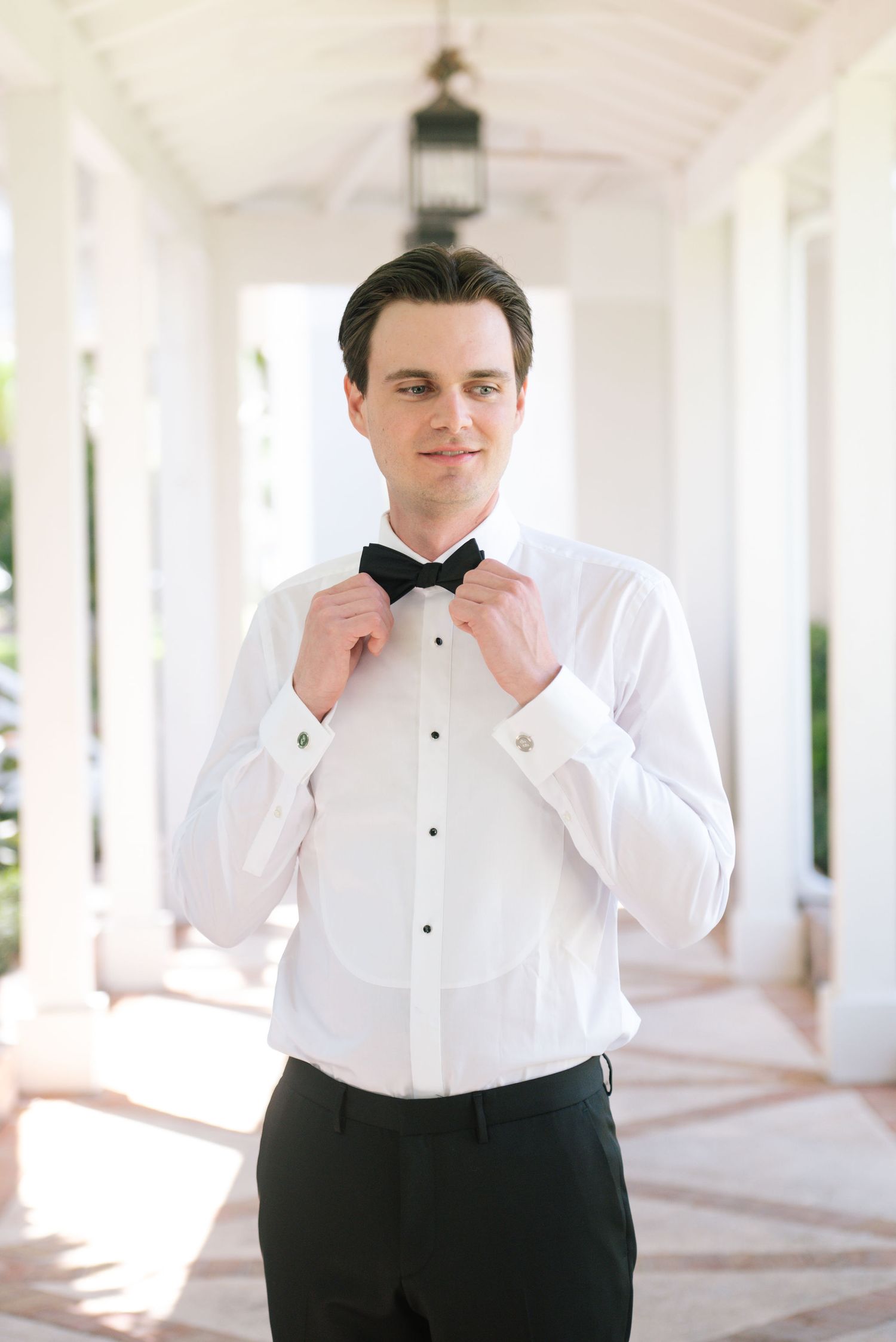 Formal wedding attire preparation in a bright white colonnade hallway.