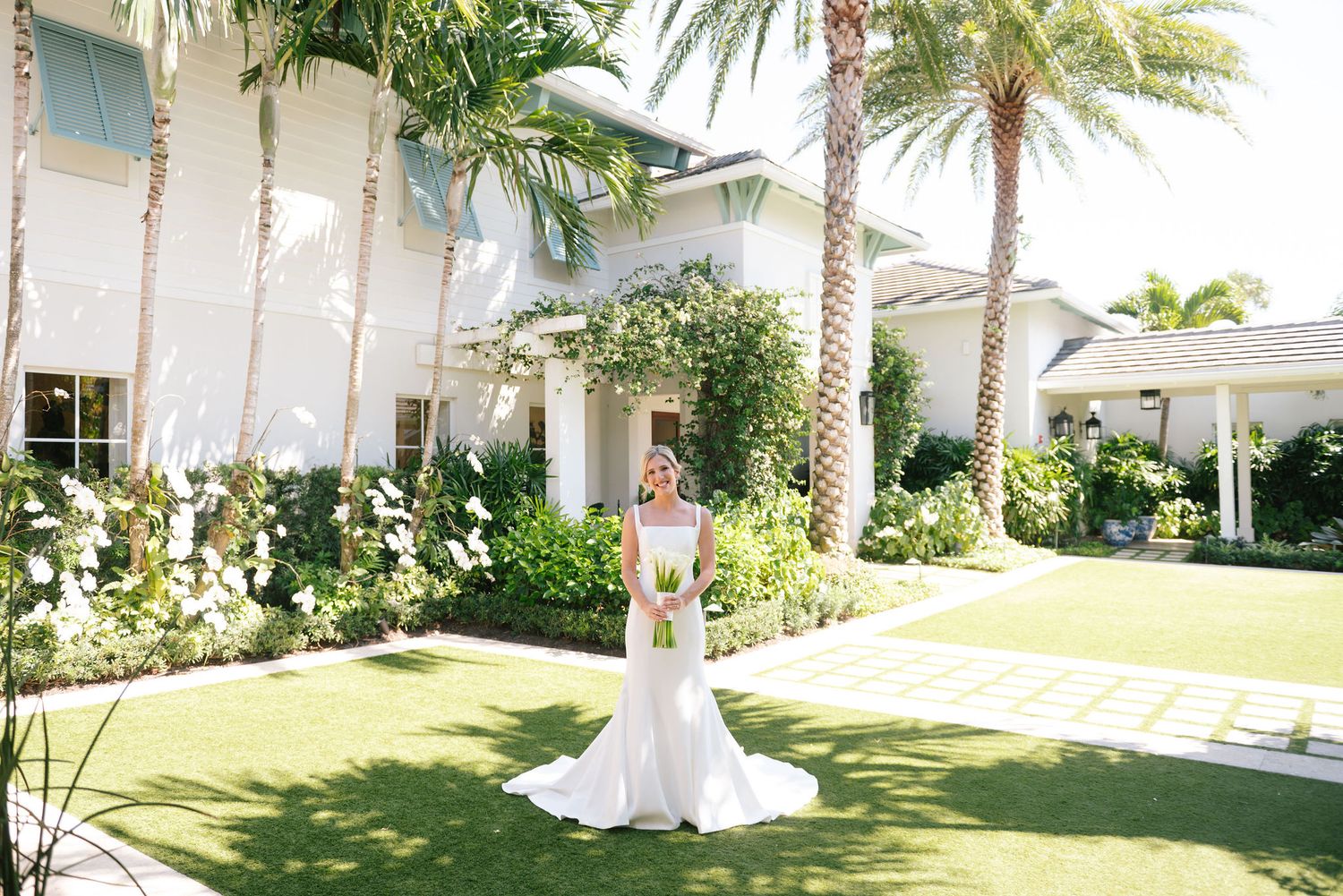 Bridal portrait on manicured lawn with white colonial style building and palm trees.