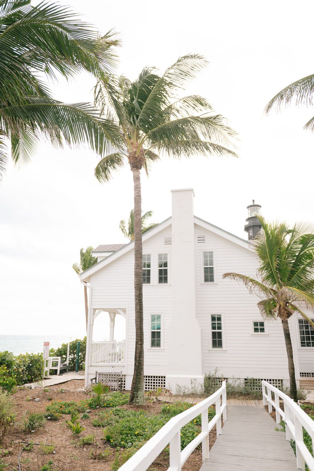White coastal house with wraparound porch and palm trees swaying in the tropical breeze.
