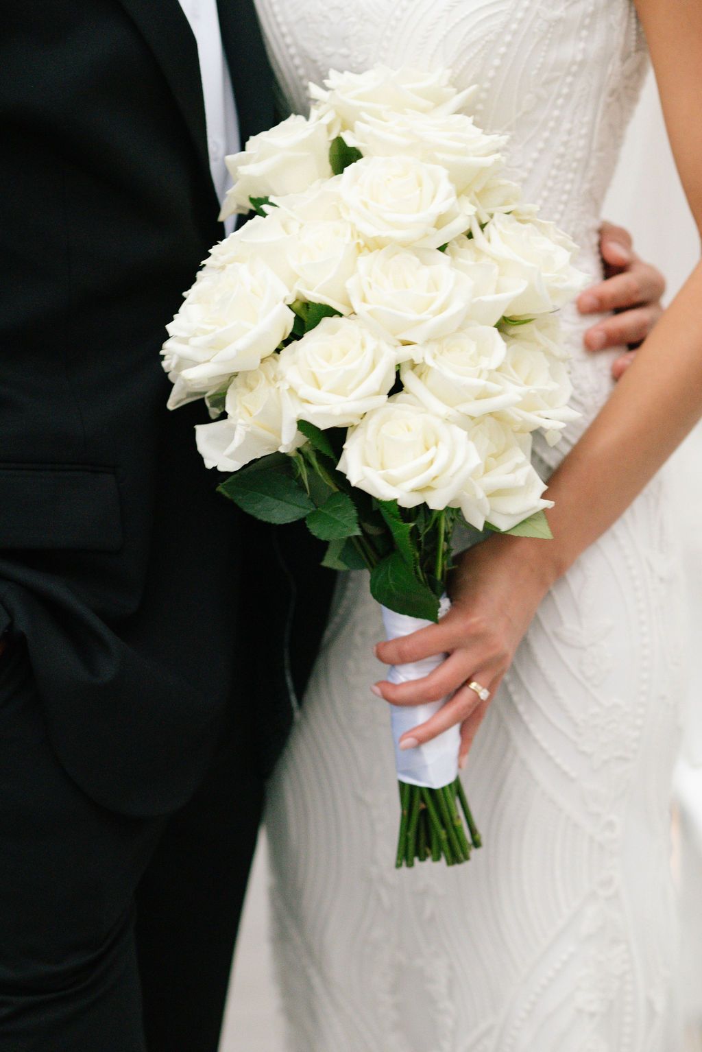 Close-up details of white rose wedding bouquet against bridal gown.
