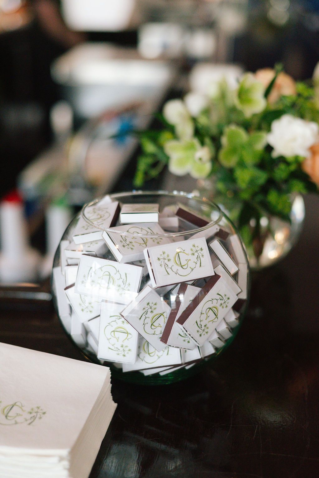 Glass bowl filled with white paper cards on a dark wooden table with floral arrangement.