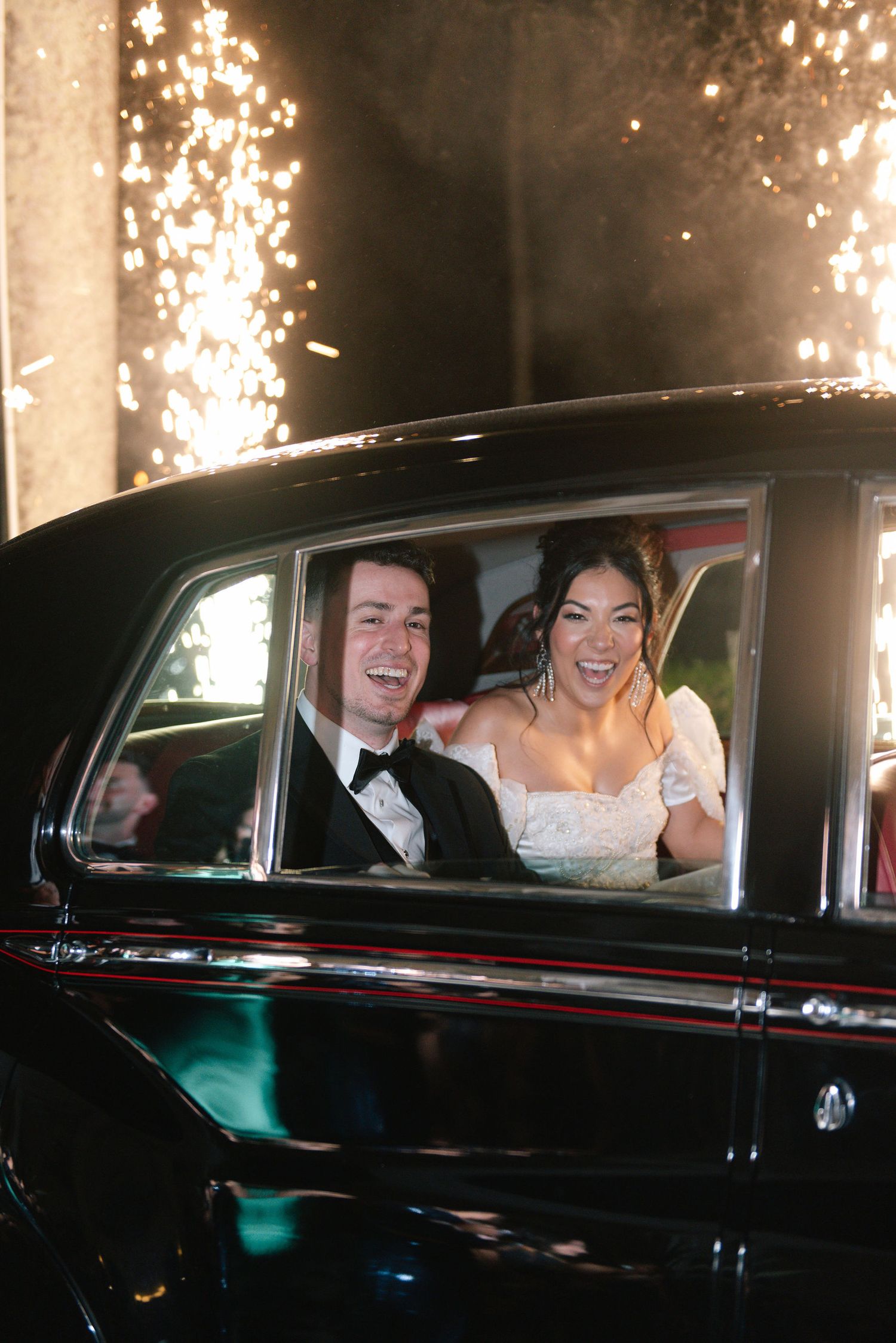 Classic black car with sparklers creating a dramatic exit scene at night.