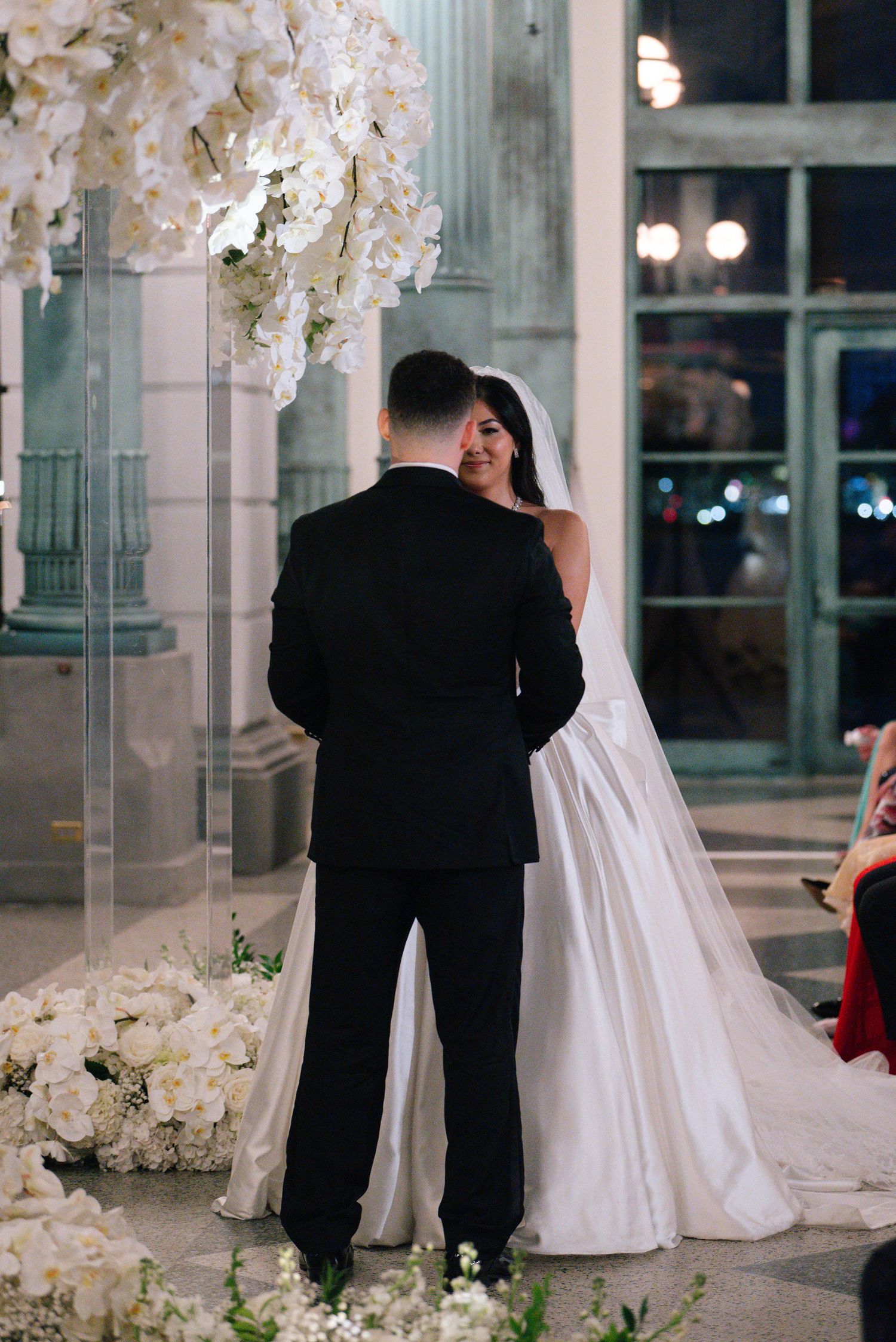 Wedding ceremony under elegant white floral arrangements and crystal chandeliers.