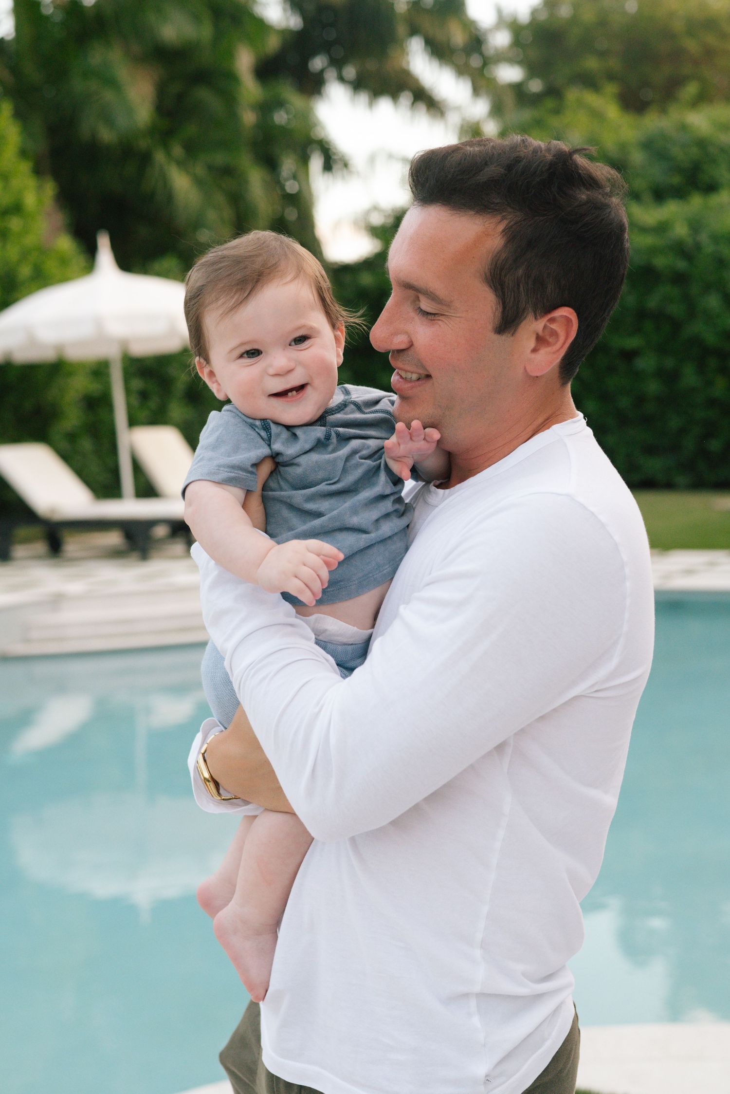 A tender moment of parent and child embracing by a swimming pool on a sunny day.