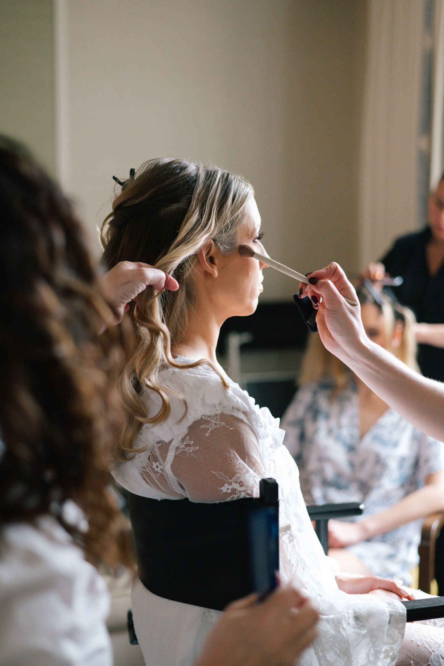 Wedding preparation scene showing makeup application with white lace details and natural lighting.