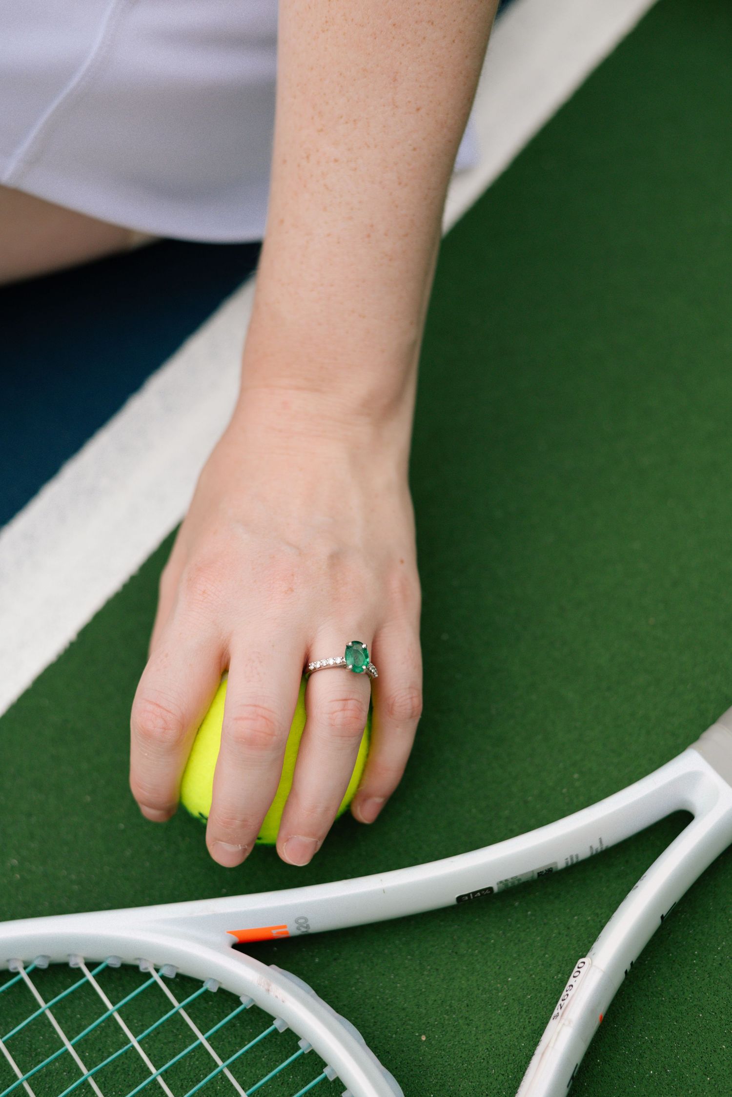 Close-up of hand with ring touching white tennis racket strings.