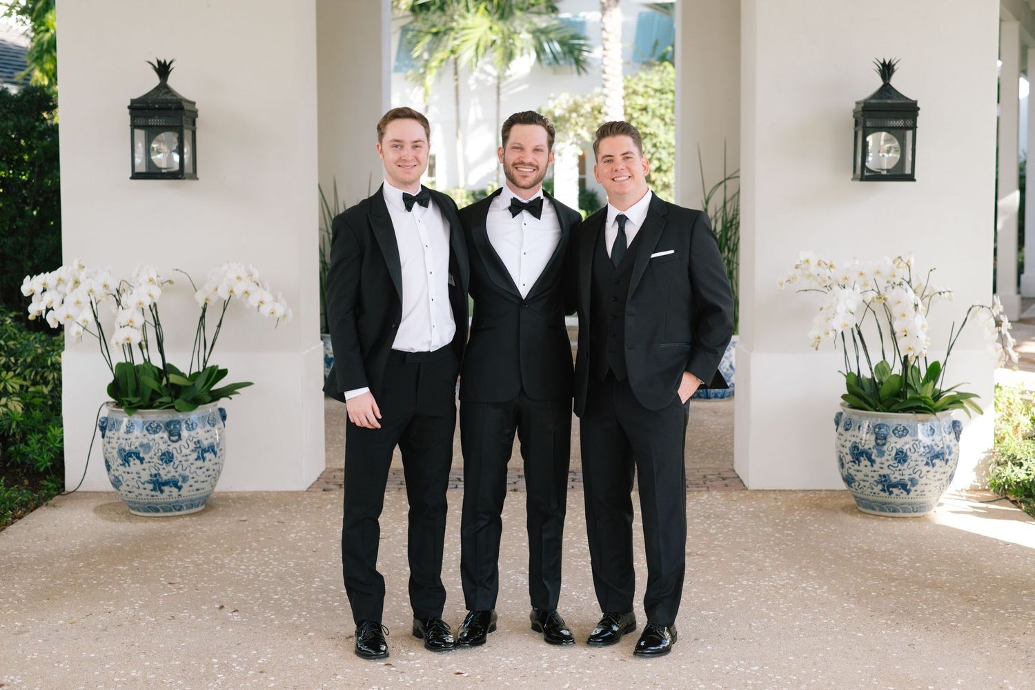 Groomsmen in black tuxedos and bow ties pose together at an elegant outdoor venue.