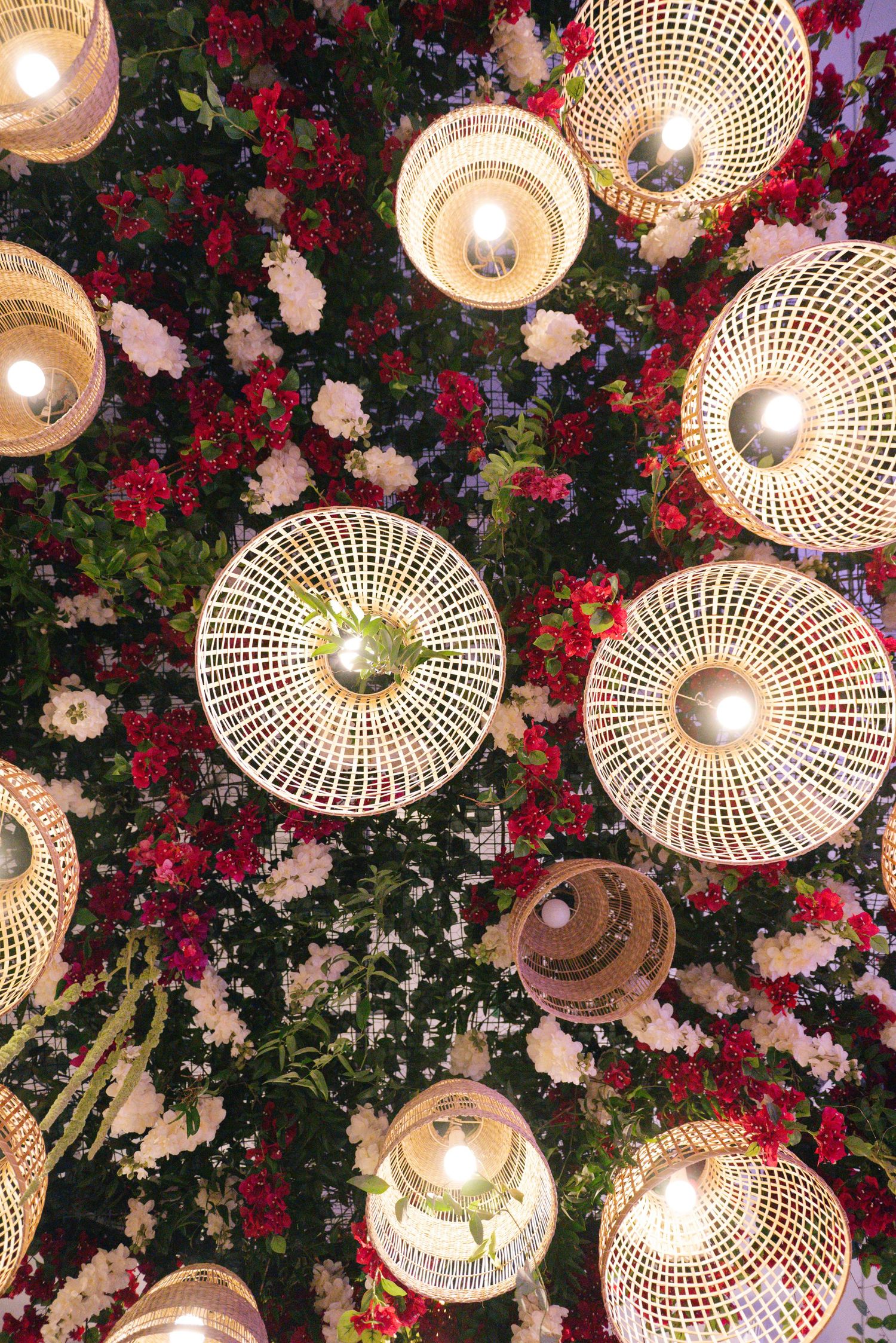 Decorative woven light fixtures hanging among red and white flowers creating a romantic ambiance.