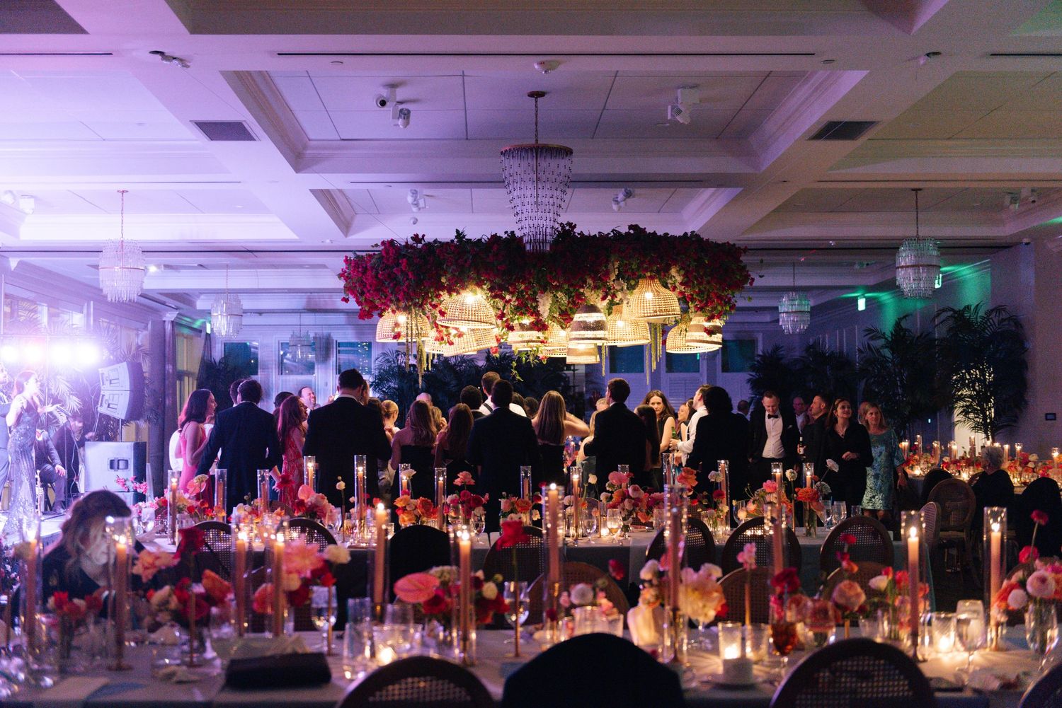 Dimly lit reception ballroom with dramatic floral ceiling installation and glowing candlelit tables.