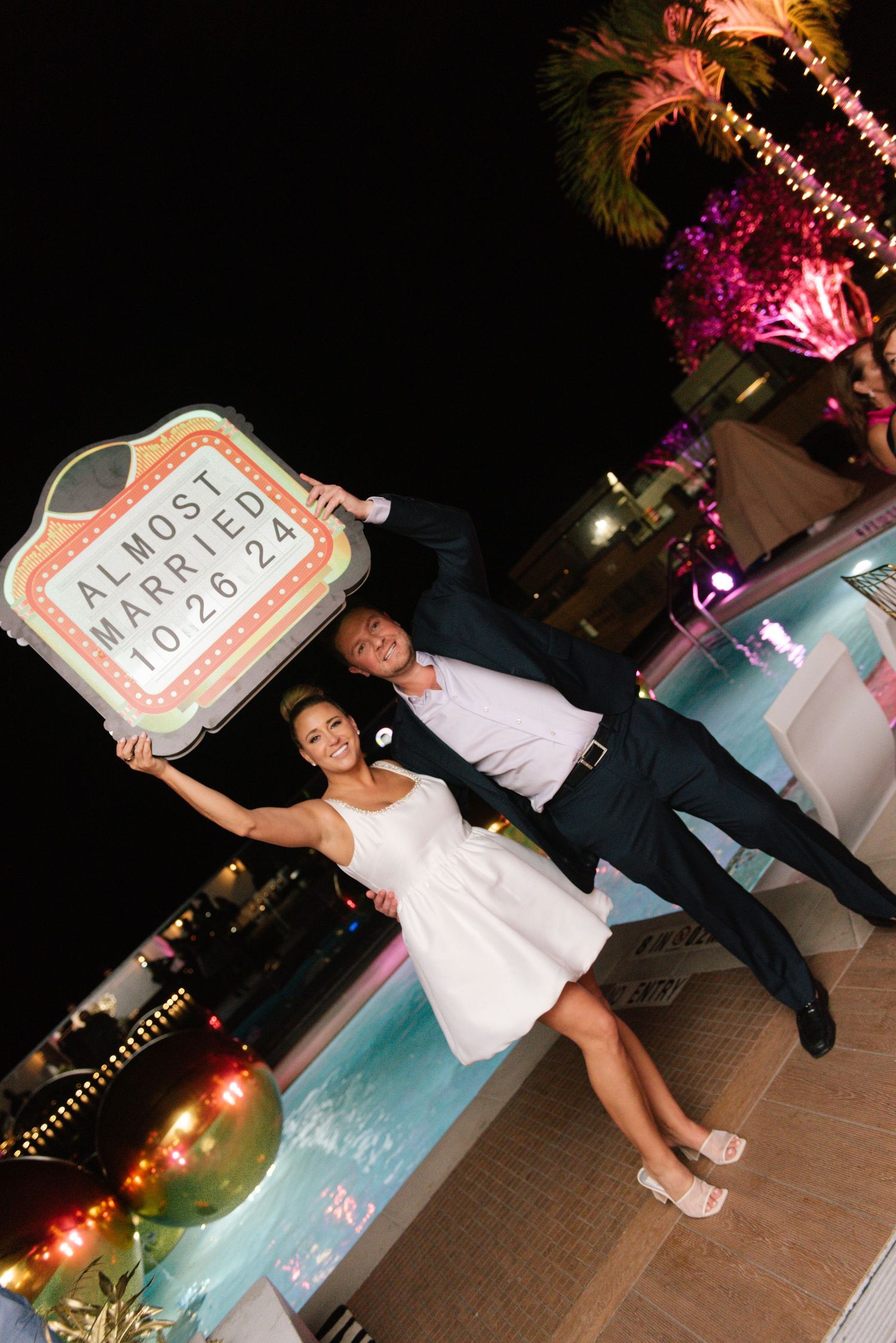 Engagement celebration photo with 'Almost Married' sign by a poolside.