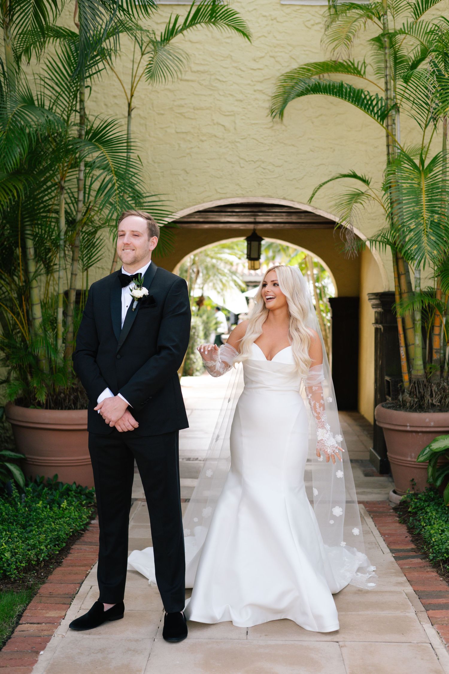 Wedding couple poses in a tropical courtyard surrounded by palm trees and arches.