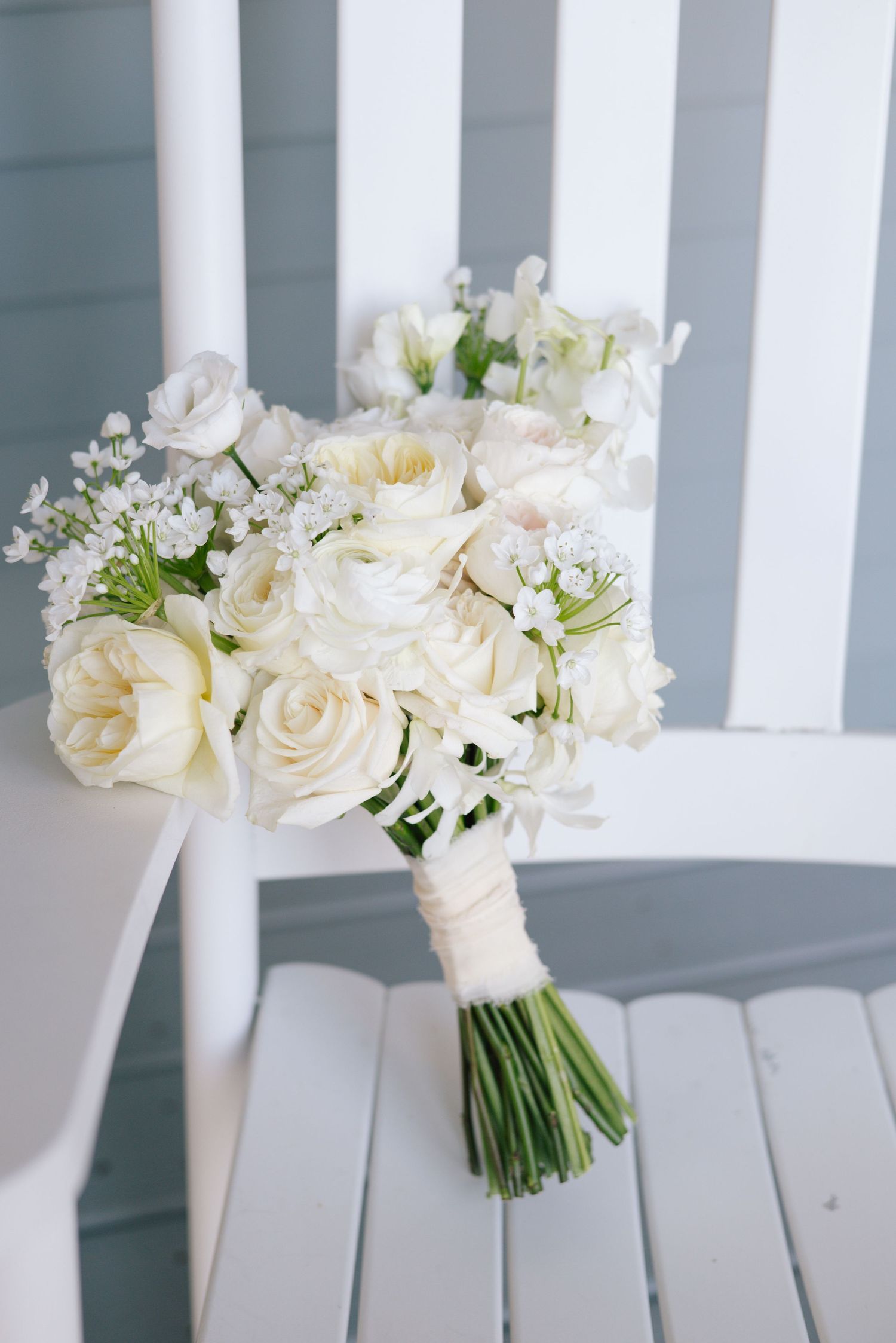 Elegant white rose and flower bouquets displayed on white wooden chairs.
