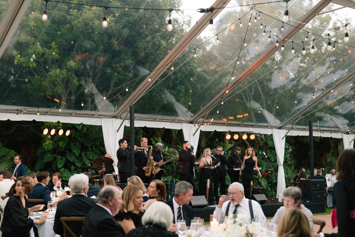 Clear tent reception with string lights and lanterns creates a romantic outdoor wedding atmosphere.