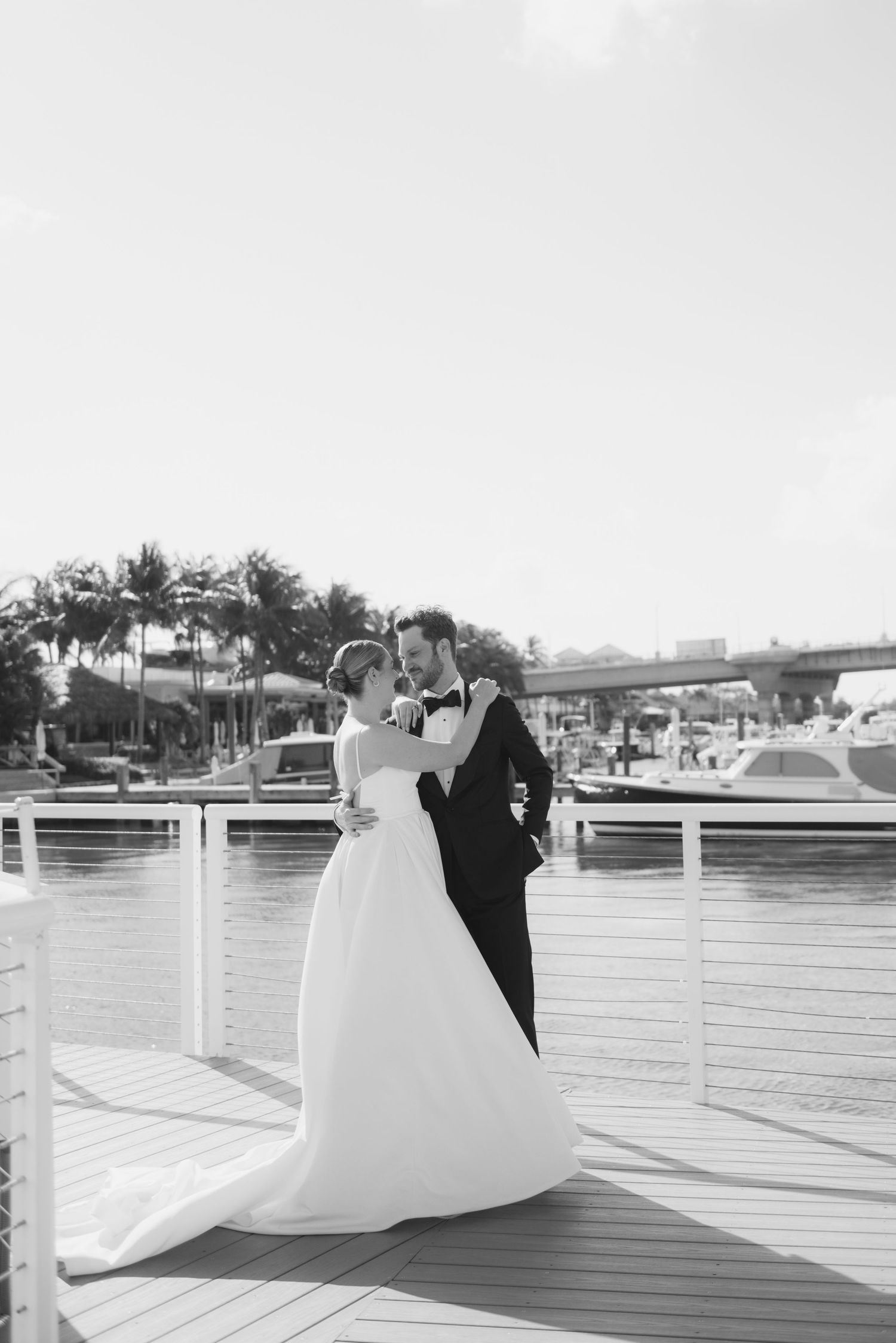 Wedding couple on a waterfront deck with boats and palm trees in the background.