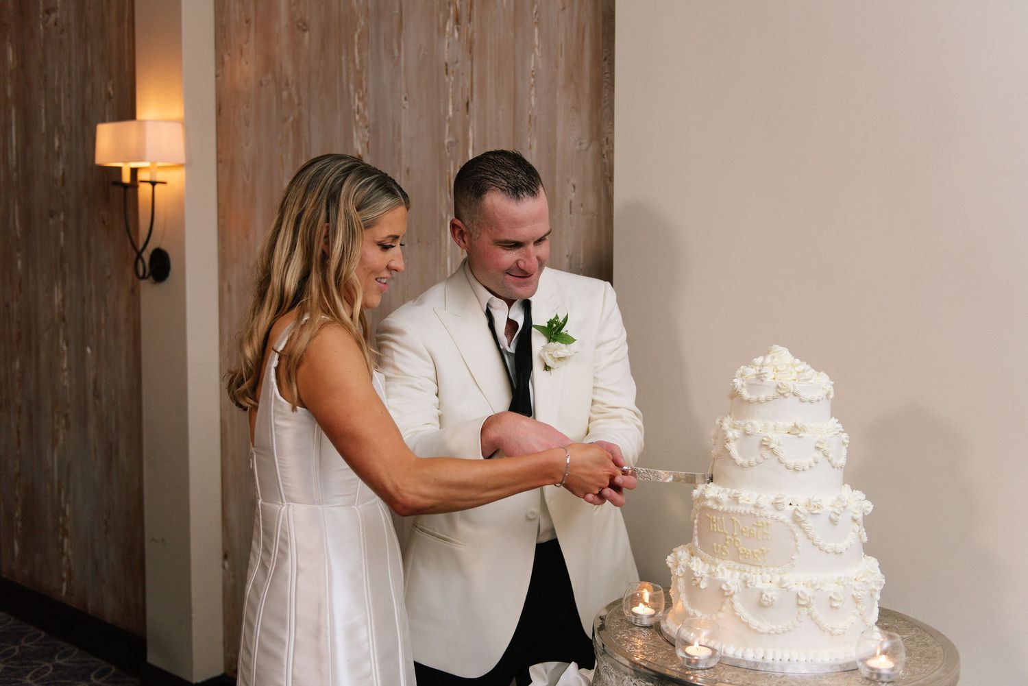 Wedding cake cutting scene with a white tiered cake decorated with delicate frosting details.