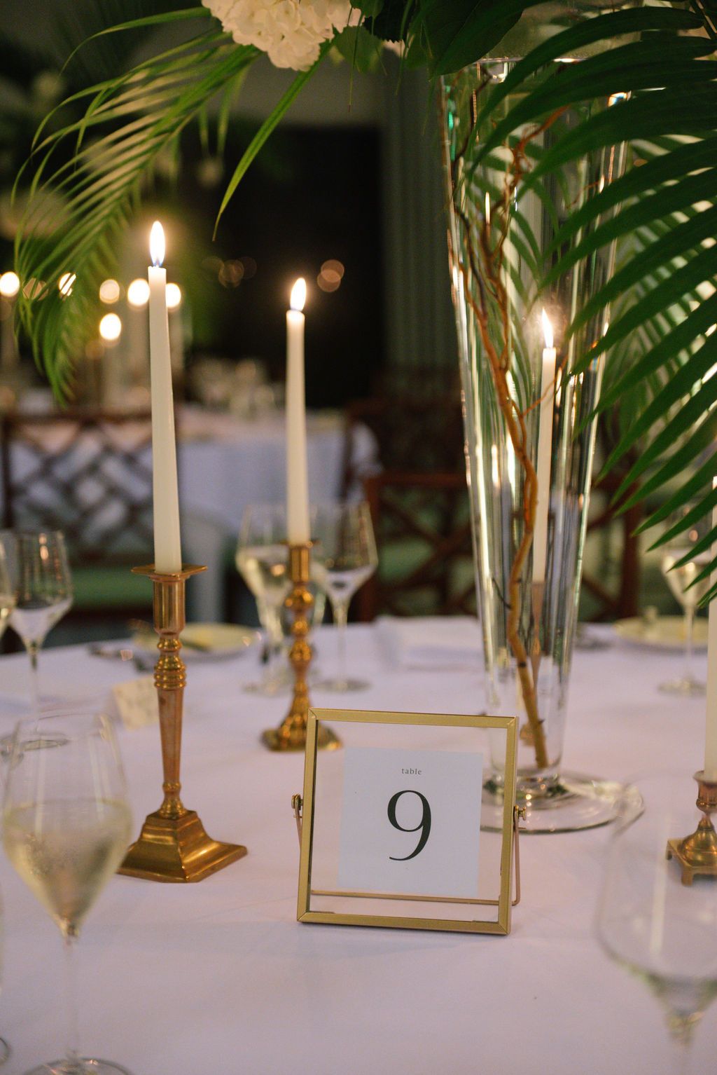 White table settings with gold candelabras and palm decor at an upscale wedding reception.