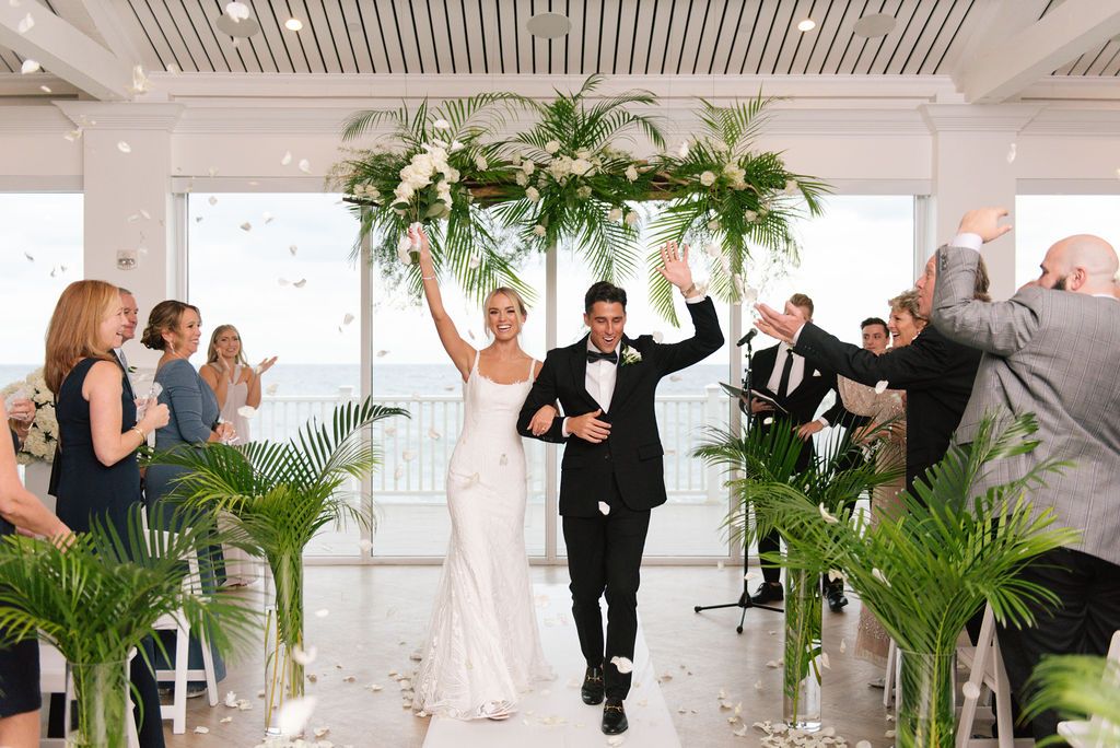 Celebratory exit of newlyweds with raised arms under tropical palm decor.