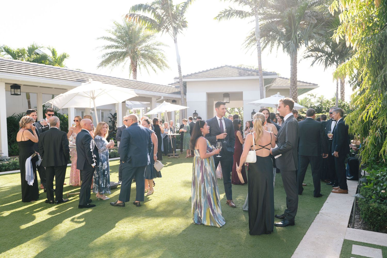 Wedding guests mingle on a palm tree-lined patio during cocktail hour.