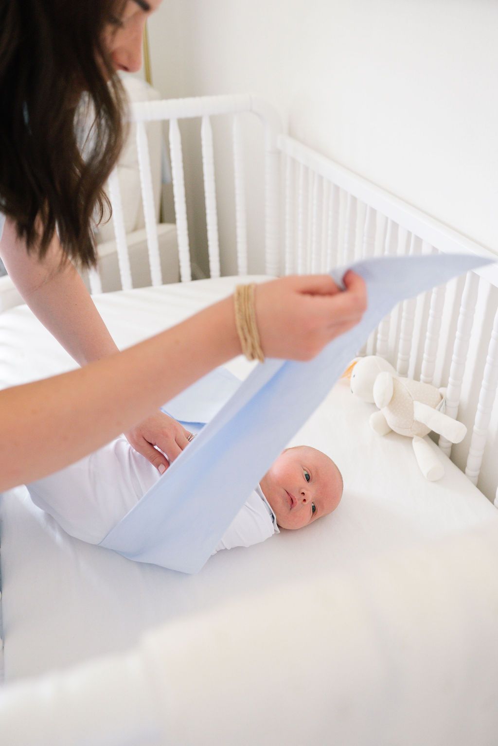 A baby lying in a white crib while being wrapped in a light blue blanket.