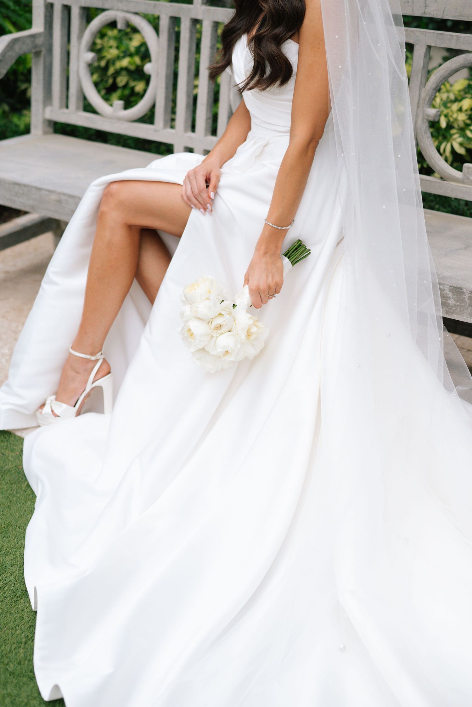 Detail shot of white wedding dress and bouquet against garden backdrop.