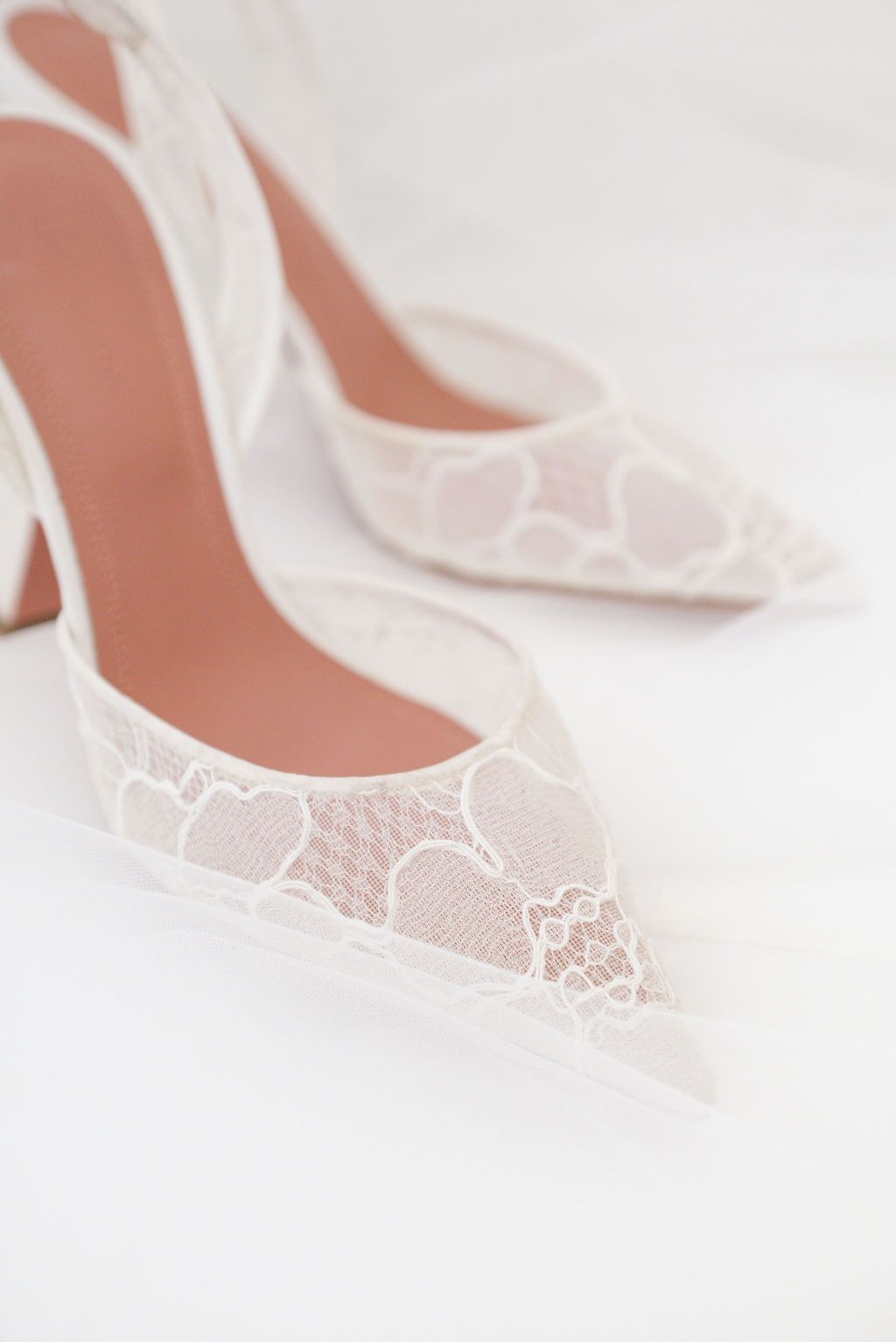 Delicate white lace bridal shoes displayed on light background.