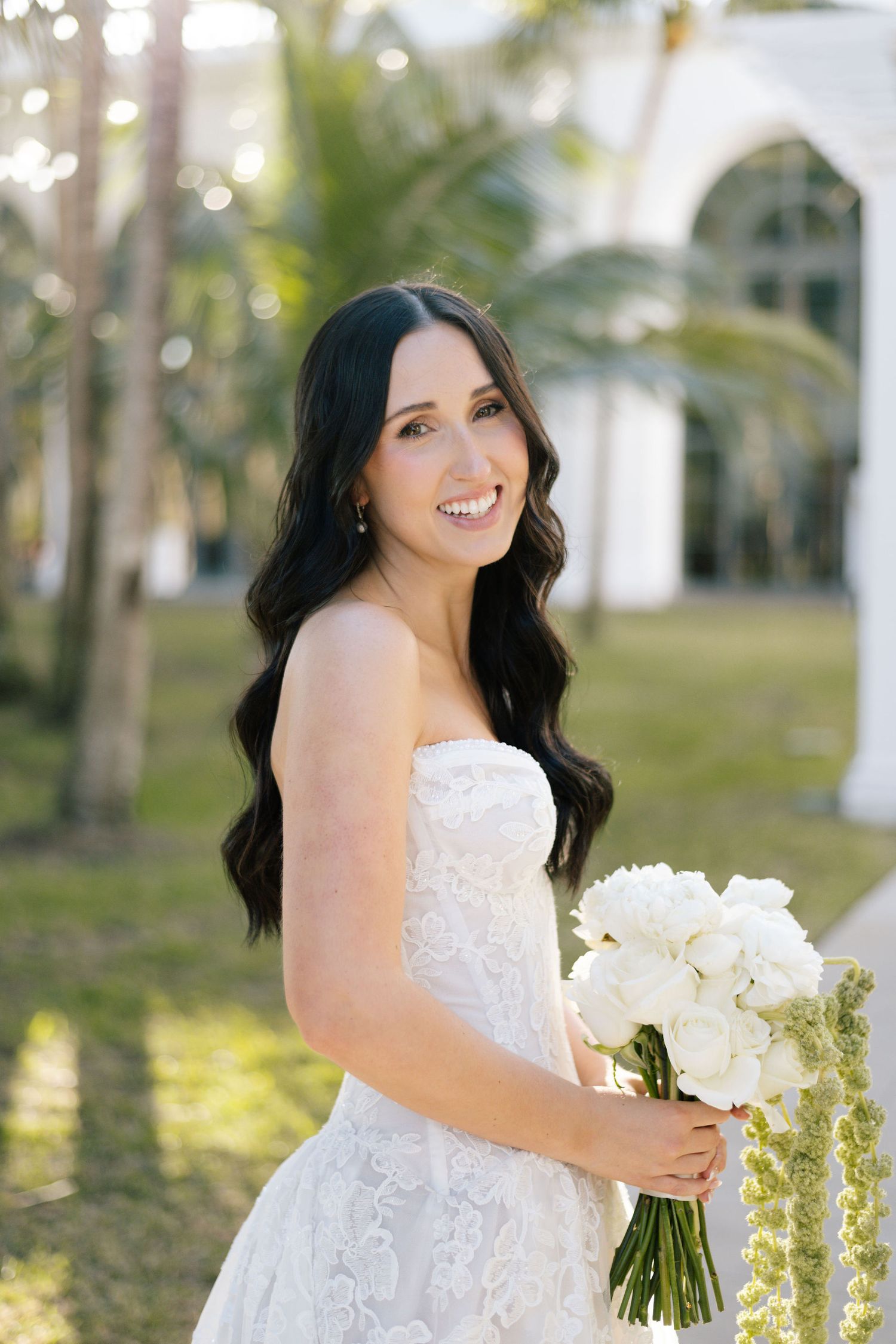 Bridal portrait with white bouquet against palm trees and white columns.