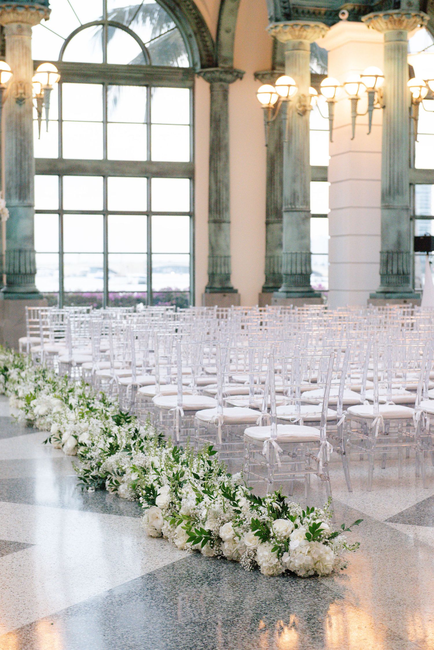 White chairs arranged in rows with floral aisle decorations in elegant ballroom setting.