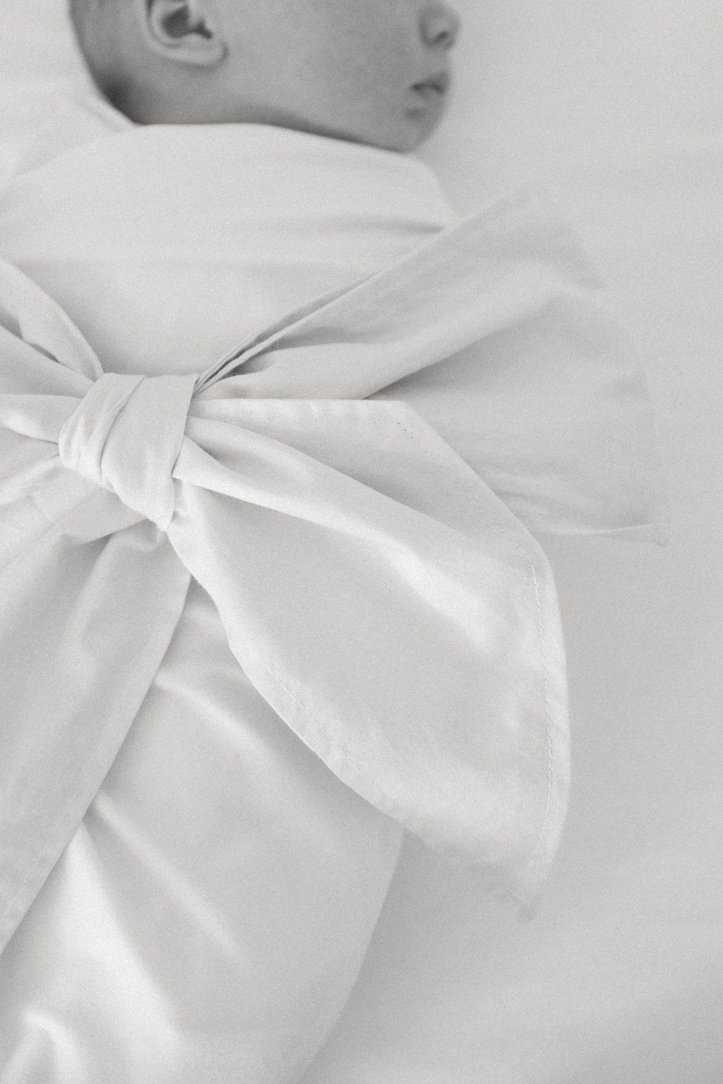 Close-up black and white photo of a large decorative bow on baby clothing.