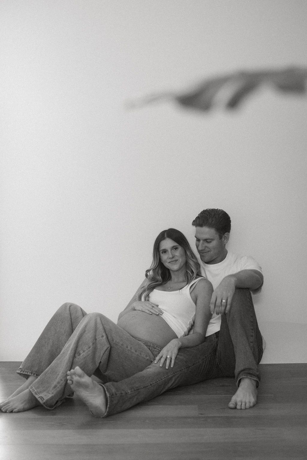 Black and white photos of a couple lying together on a wooden floor during a photoshoot.