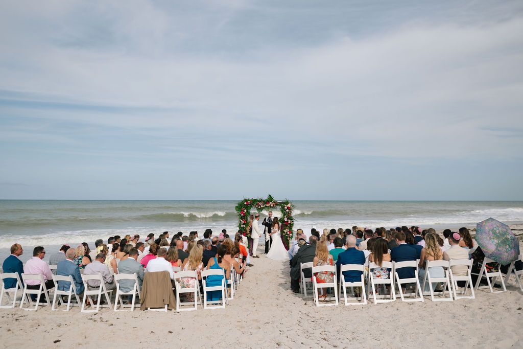 Panoramic view of white chairs set up for a beach wedding ceremony with ocean backdrop.