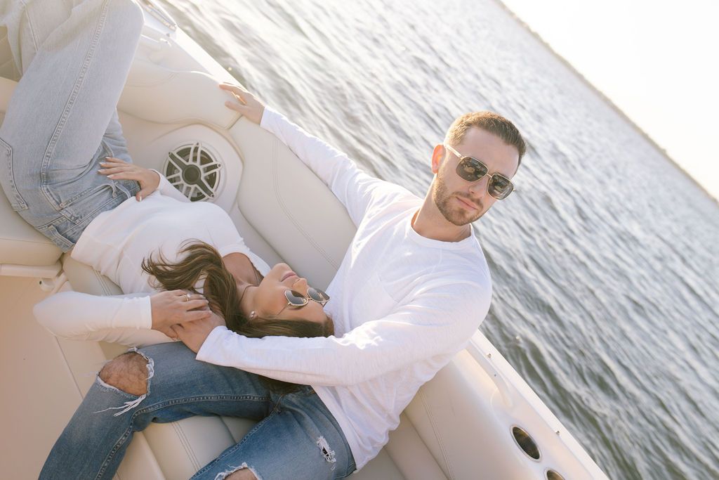 Couple sharing tender moment on boat bench with water and sunset in background.