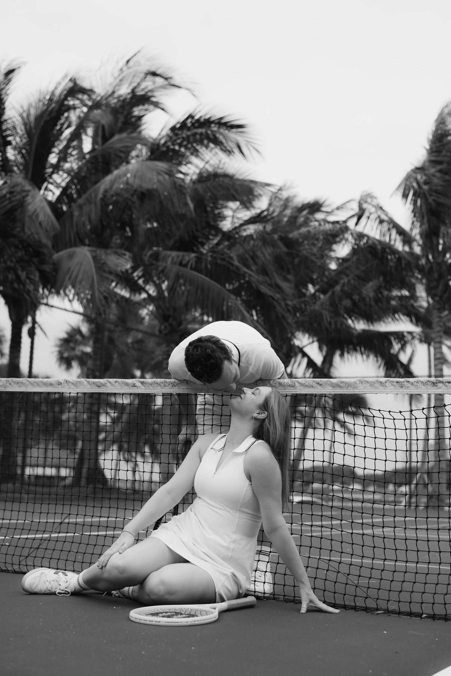 Black and white photos of a couple playfully posing on a tennis court with palm trees in background.