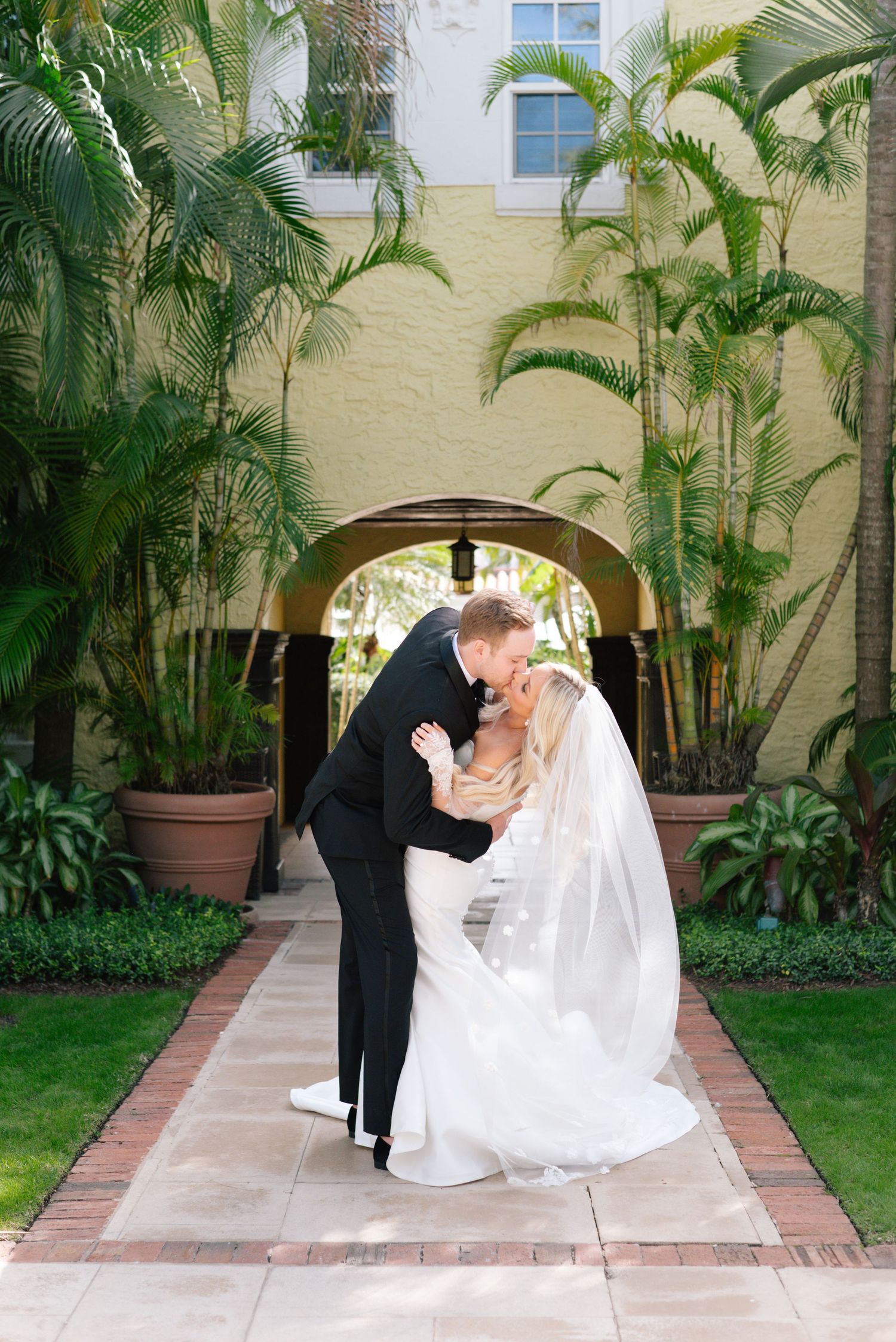 A romantic wedding moment captured in a palm-lined courtyard with Spanish architecture.