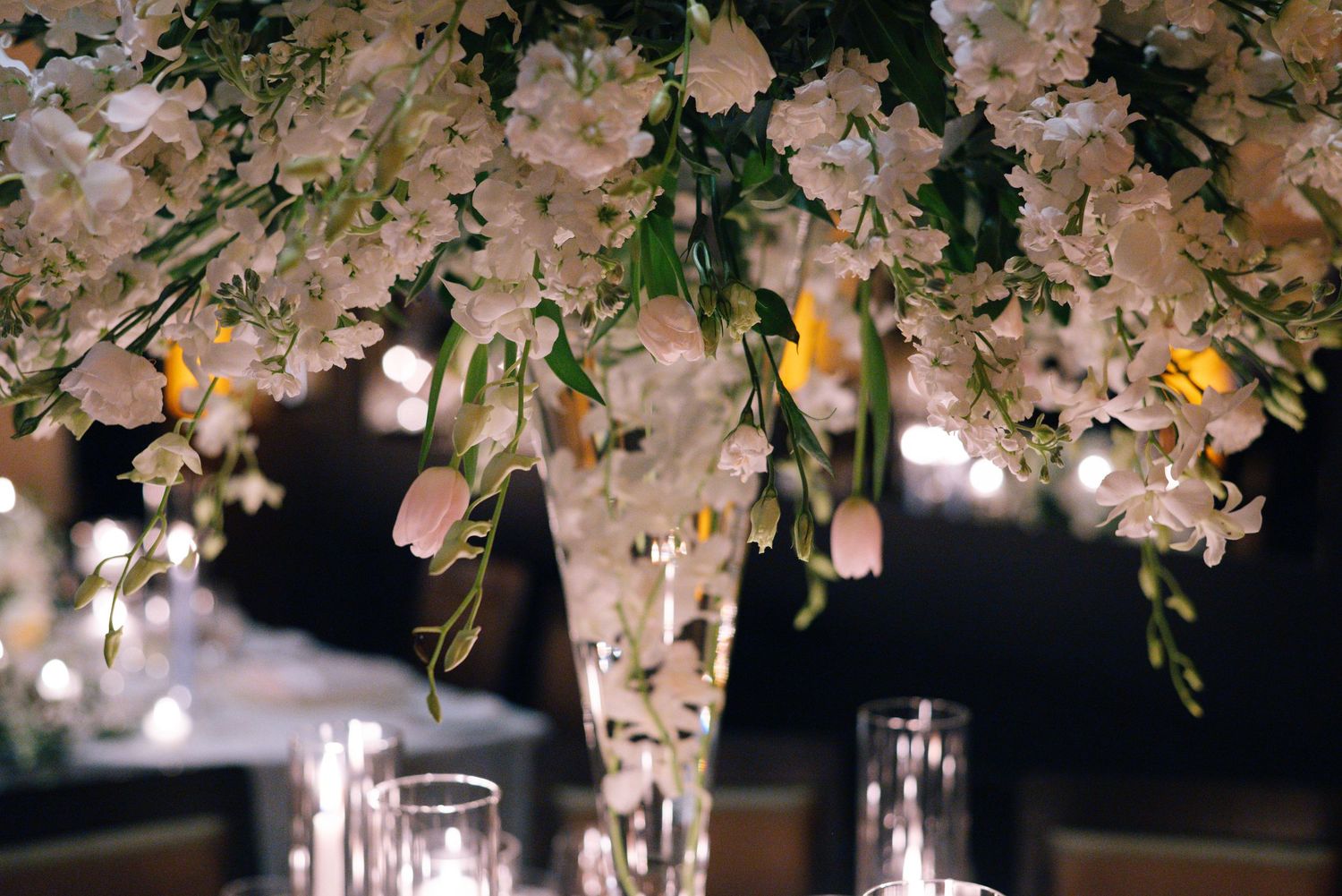 Elegant floral centerpiece with white blossoms and candlelit table settings at an evening wedding reception.
