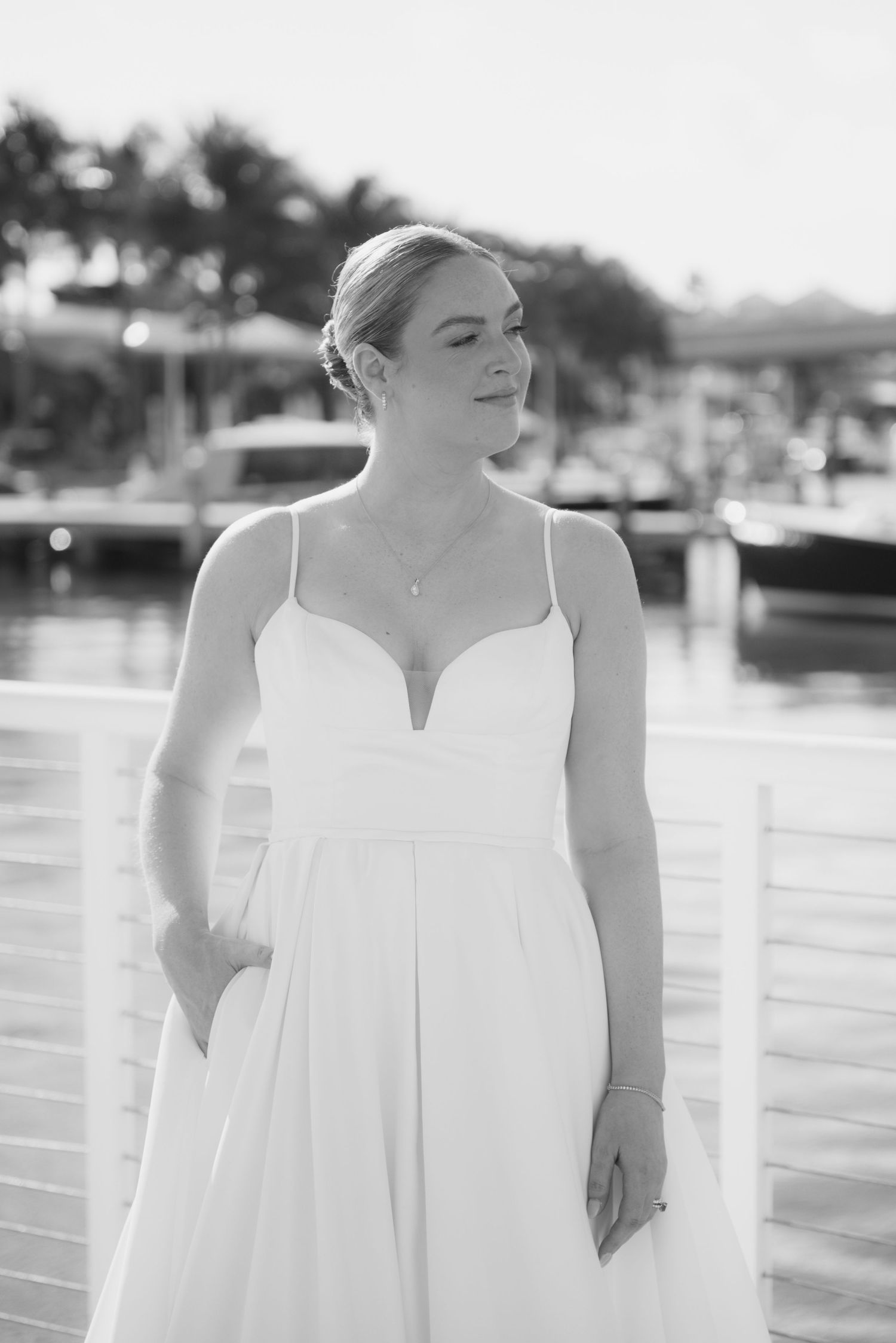 A person in a white wedding dress poses on a dock at a marina on a sunny day.