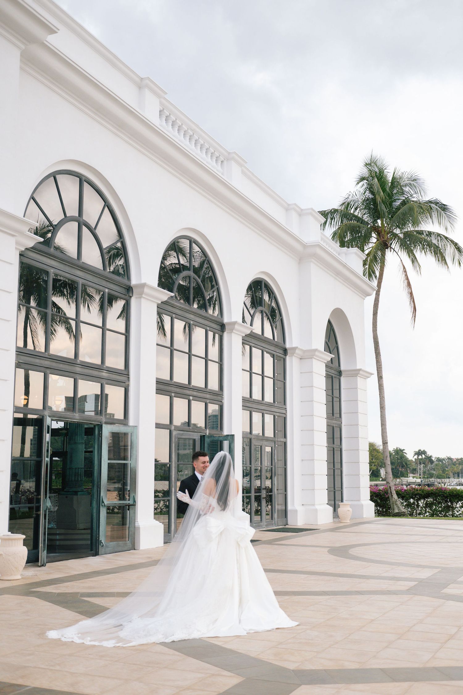 A romantic wedding photo session in front of a white colonial building with arched windows and palm trees.