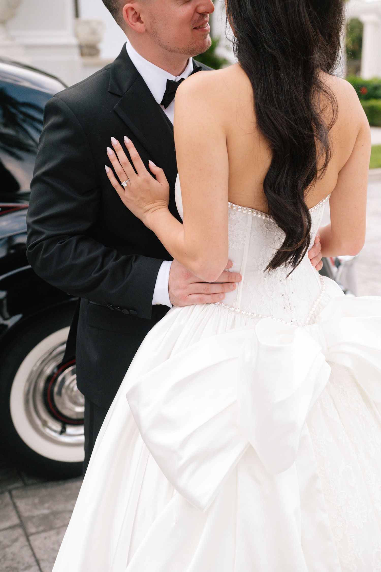 A romantic wedding portrait showing the elegant details of a white bridal gown against a dark suit.