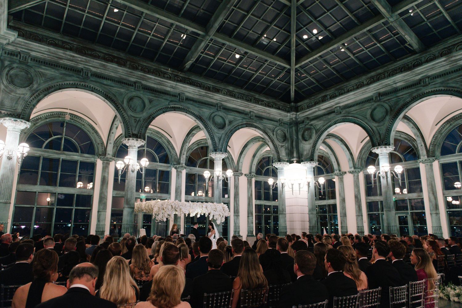 Panoramic view of an elegant ballroom wedding reception with arched windows and chandeliers.