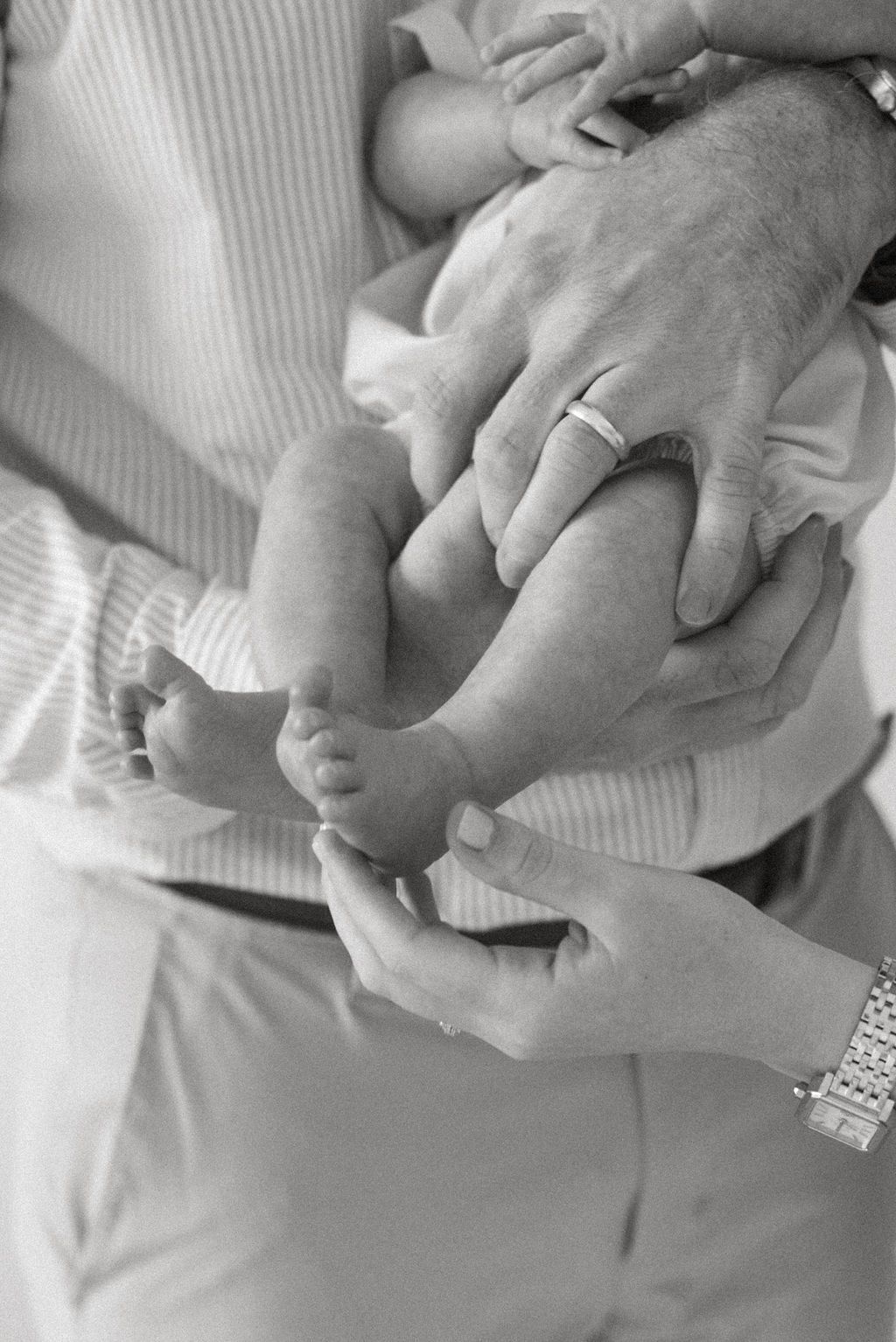 Close-up series of gentle hands holding and caressing a newborn baby's tiny fingers in black and white.