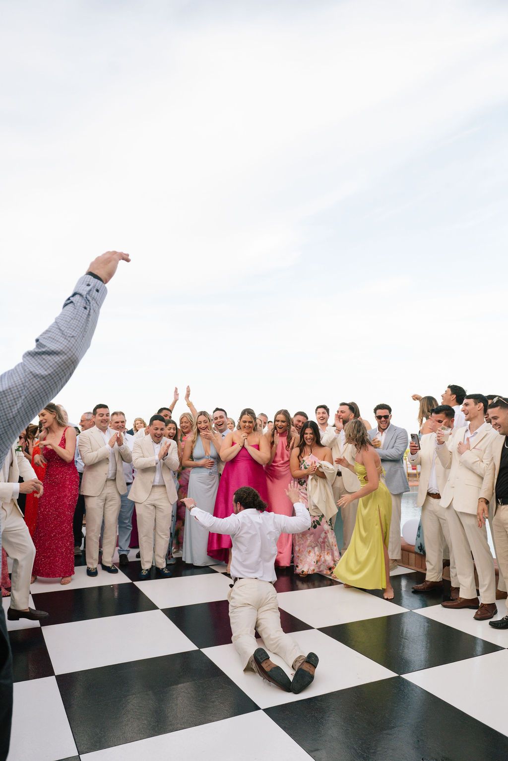 Large group of wedding guests celebrating on a black and white checkered dance floor outdoors.