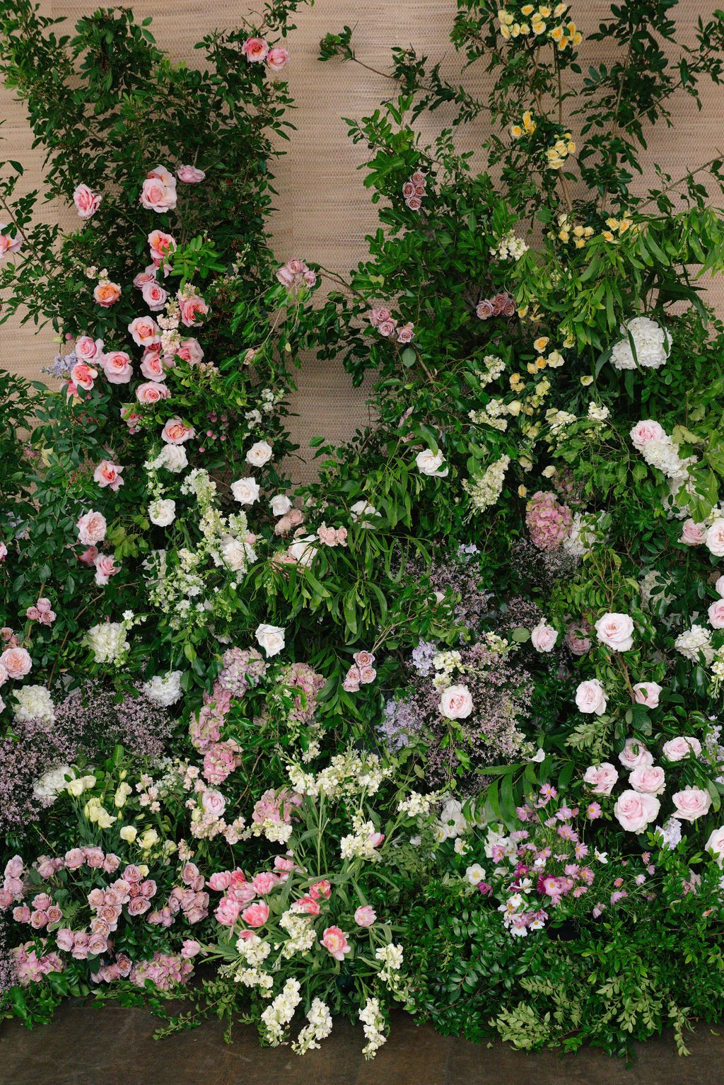 Garden-style flower wall featuring pink and white roses with abundant greenery and foliage.