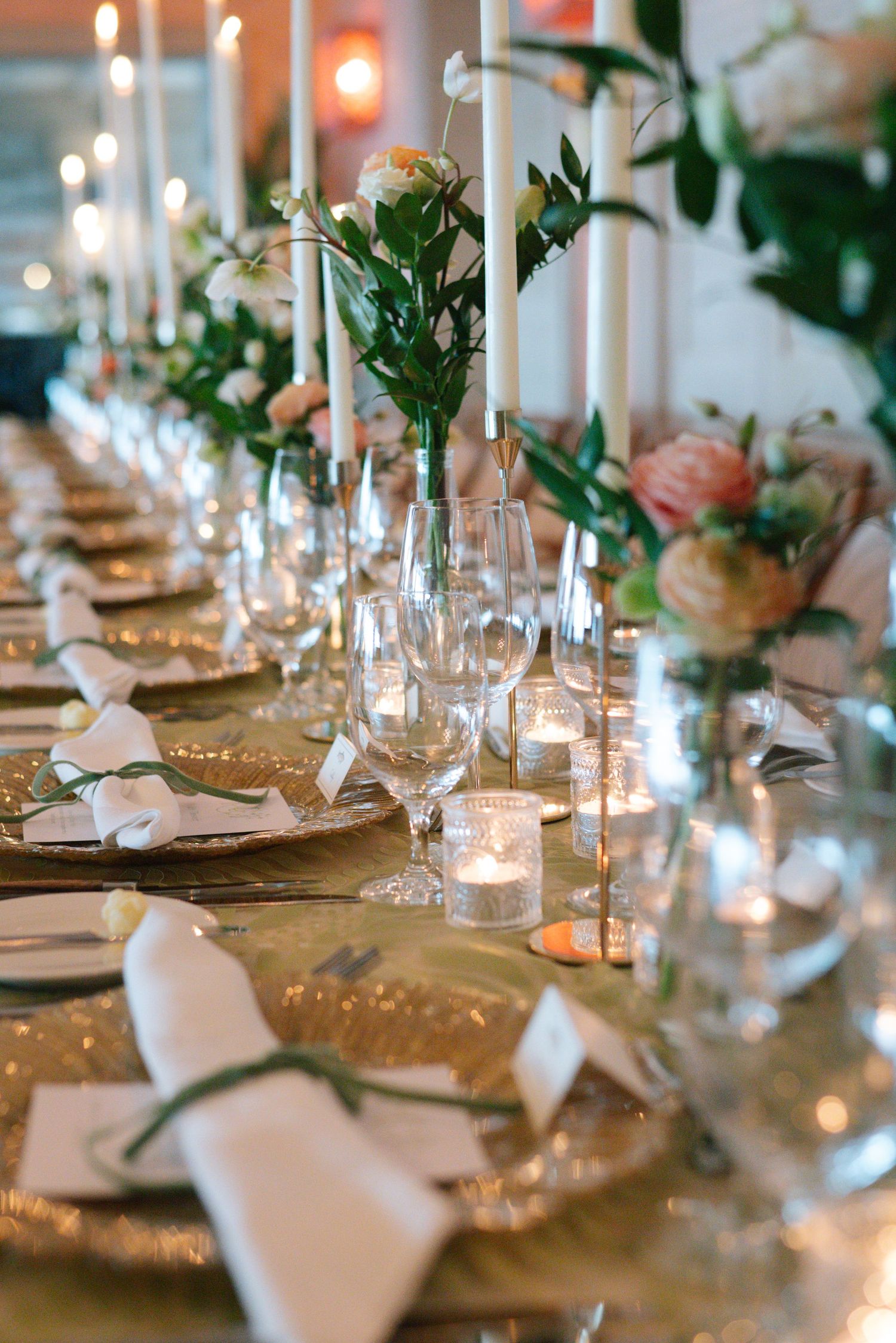 Romantic table setting with gold accents, white tapered candles and fresh floral arrangements in glass vases.