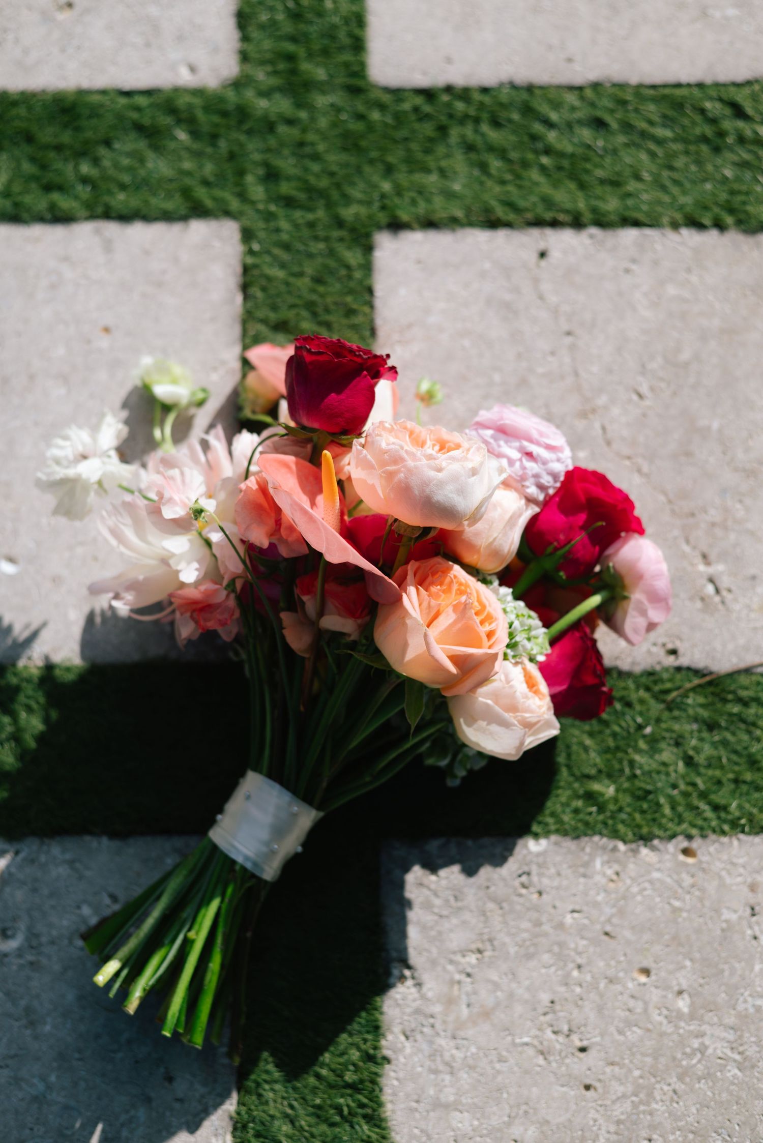 A beautiful bouquet of pink, red, and white roses arranged together against a concrete and grass background.